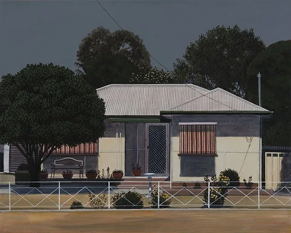 A small house with a white roof, yellow and gray walls, surrounded by trees and bushes, with a white fence in front.