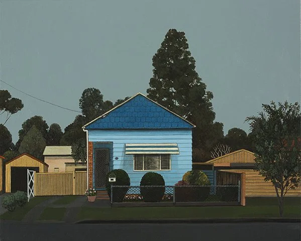 A small blue house with a gabled roof, a window with blinds, and a front door, surrounded by a black fence and landscaped yard, with large trees and neighboring houses in the background.