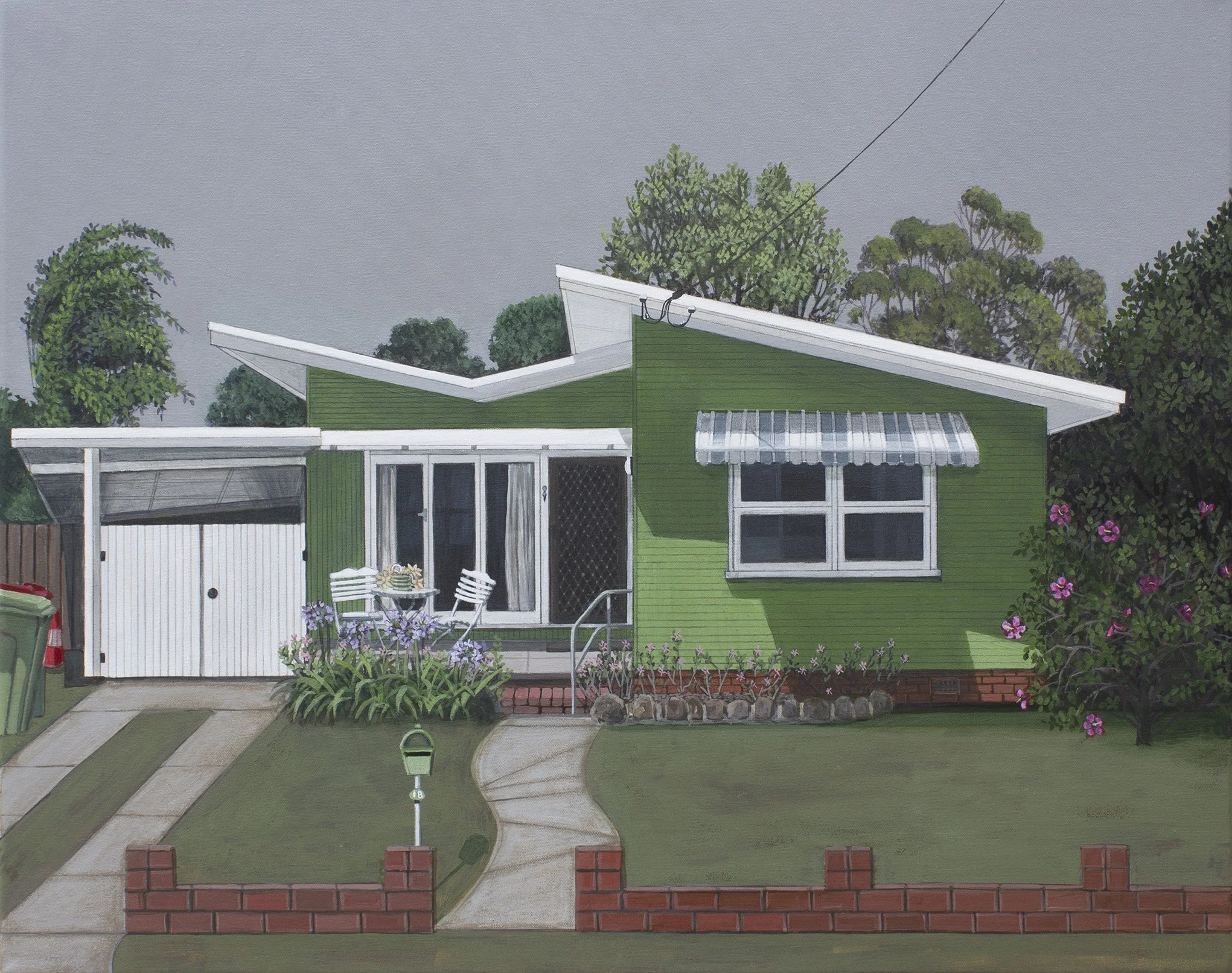 A house with a green exterior and distinctive modern roof design, surrounded by trees, with a small front yard, a driveway, and some outdoor furniture.