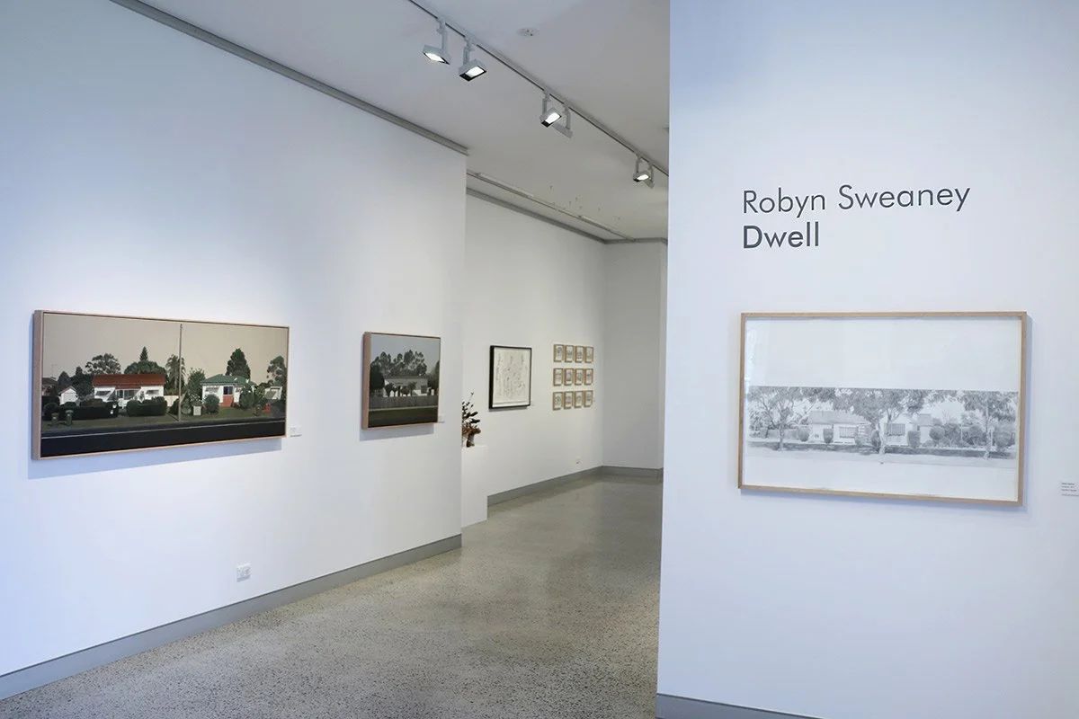 Gallery wall with paintings and photographs, including a black and white landscape, in an art gallery.
