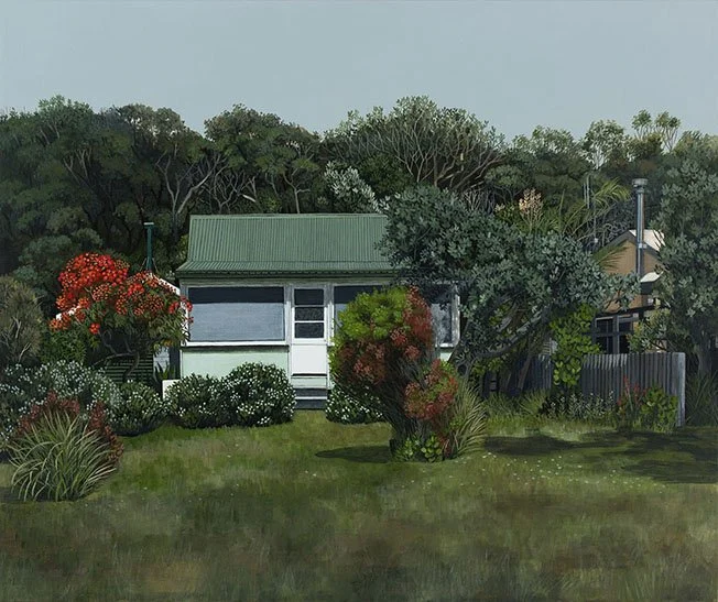 A small house with a green roof and white exterior, surrounded by lush bushes and trees in a garden, with a grassy yard in the foreground.