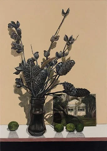 Vase with dried lavender and other plants, a picture frame, and three limes on a table against a beige wall.