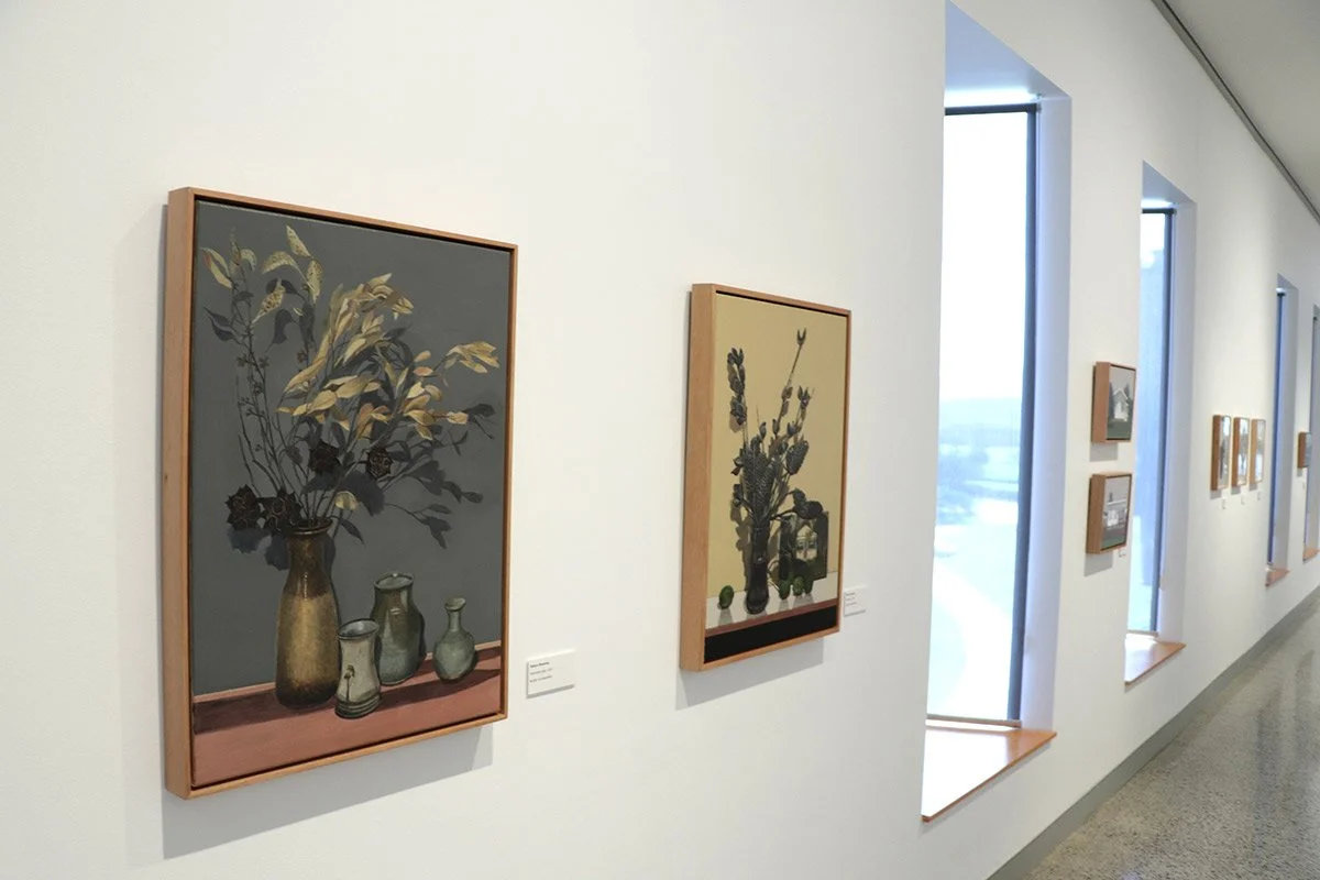 Art gallery wall with framed paintings of vase arrangements, displayed near large windows in a bright room.