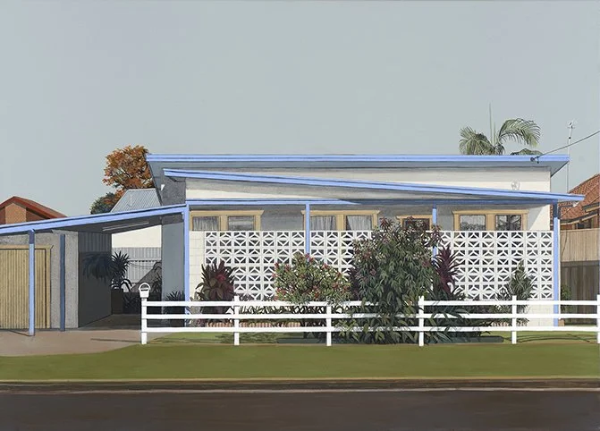 A modern house with a blue and white exterior, a sloped roof, and a white picket fence in front, surrounded by plants and trees.