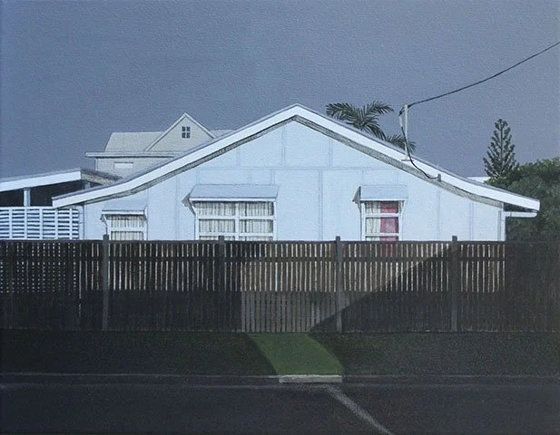 A white house with a gable roof, three windows with blinds, and a wooden fence in front. There are trees and a power line in the background.