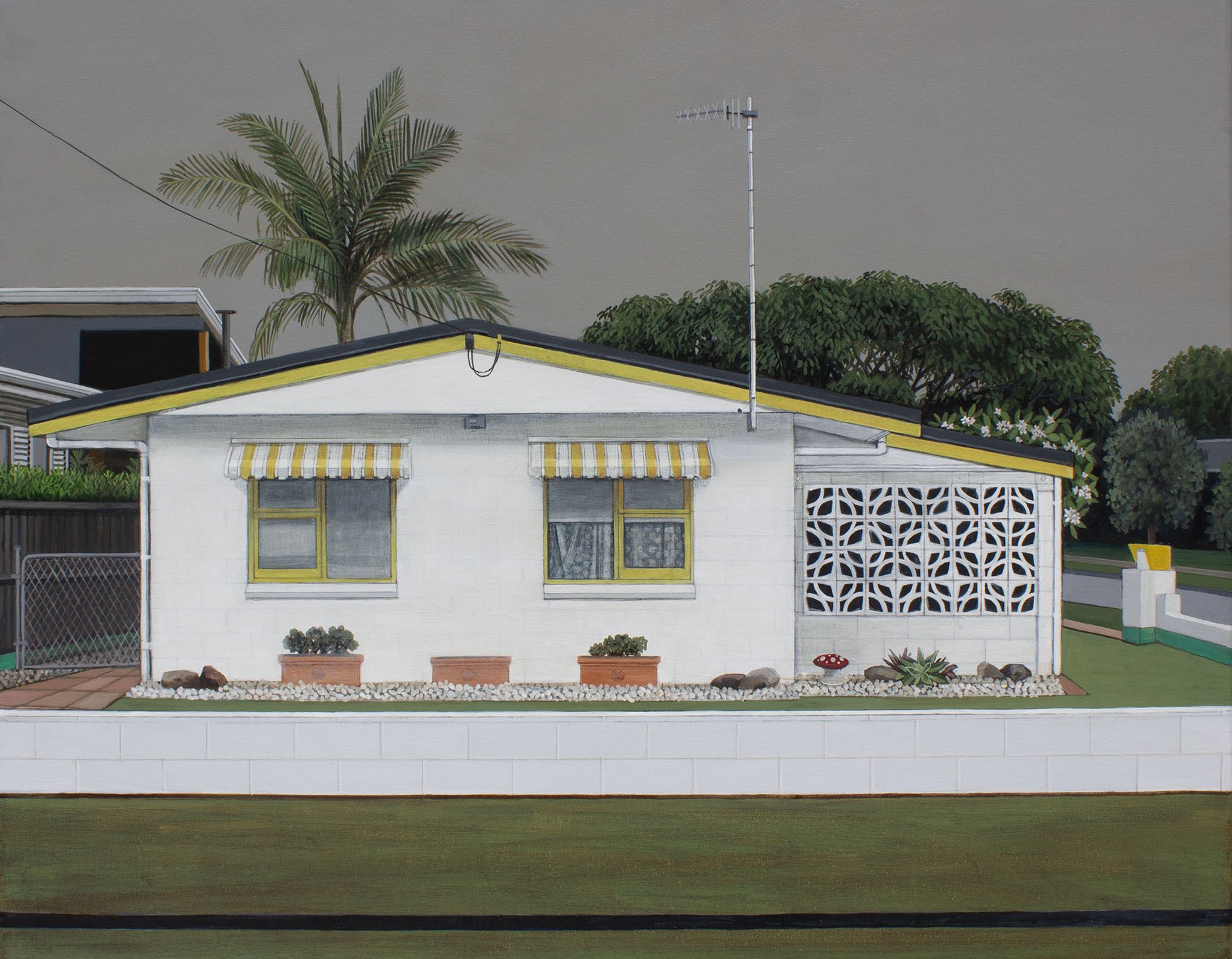 A white house with yellow trim and a striped yellow awning over the front windows. There are potted plants and decorative rocks in the front yard, with a walkway and a grass lawn. A chain-link fence is visible on the left, and a large palm tree and b