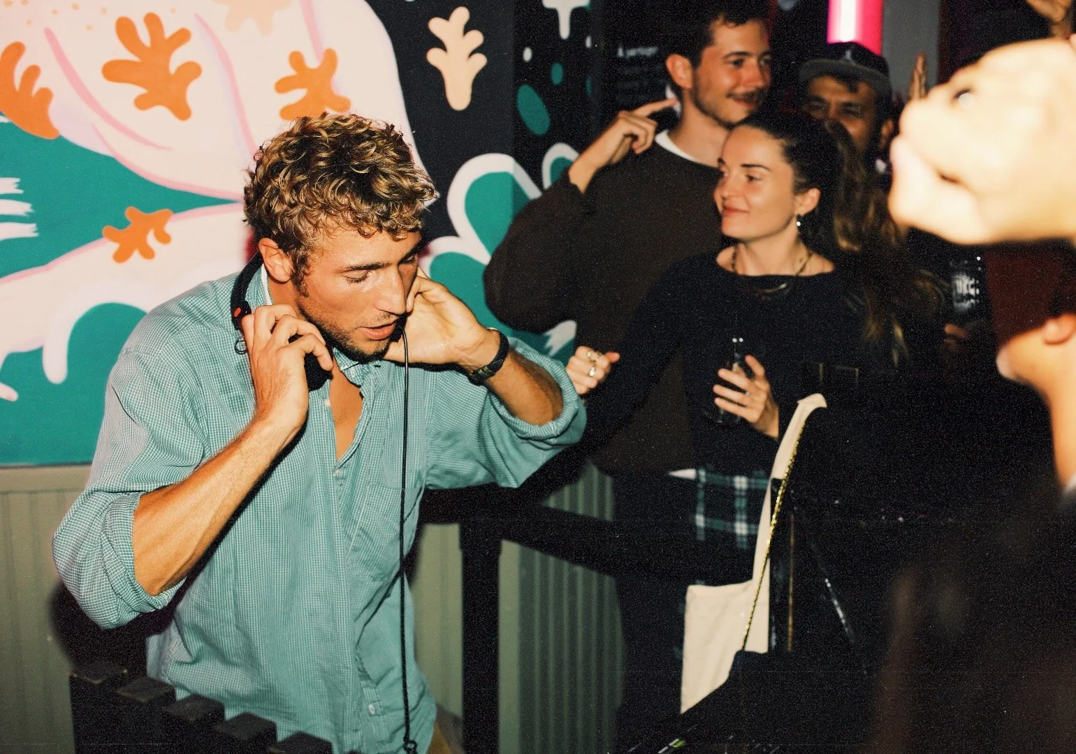 Un DJ avec des écouteurs joue de la musique dans une fête, entouré de quelques personnes dans une ambiance festive.