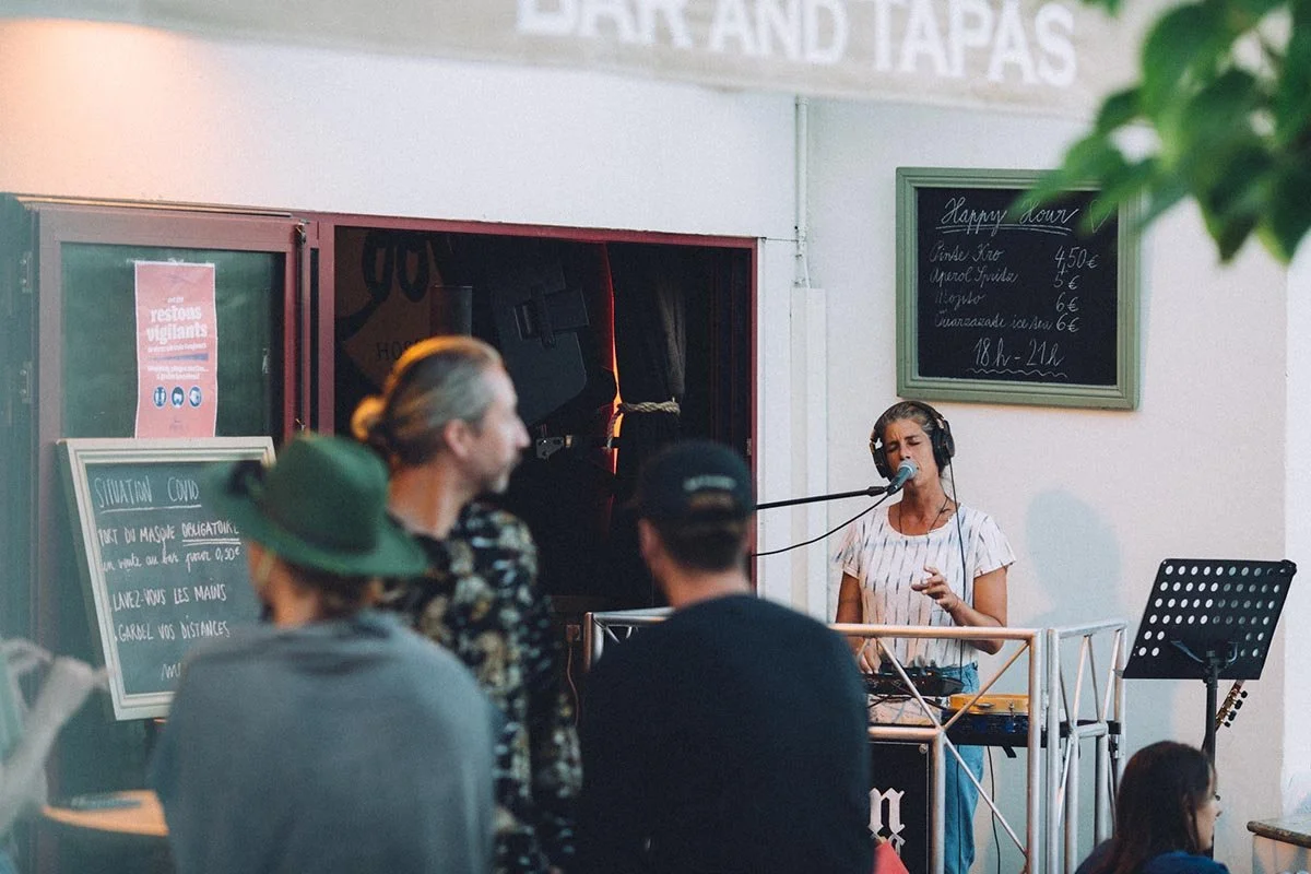 A woman is singing into a microphone, wearing headphones, standing behind a record player, in front of an audience on the terrace at Coolin