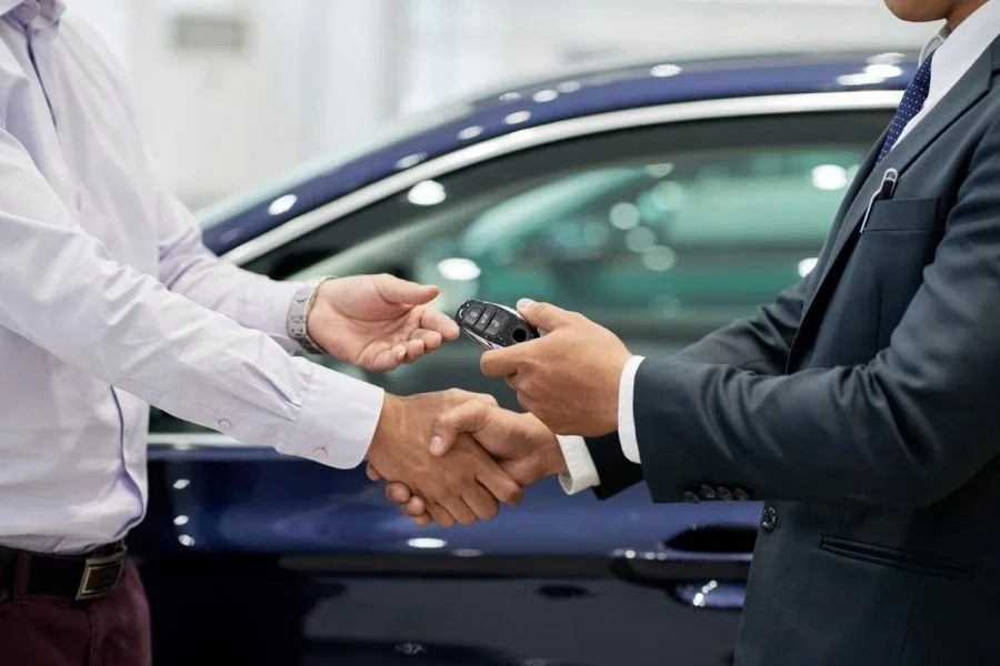 To mænd håndterer og bytter nøgler foran en bil i et bilsalg eller lease setup.