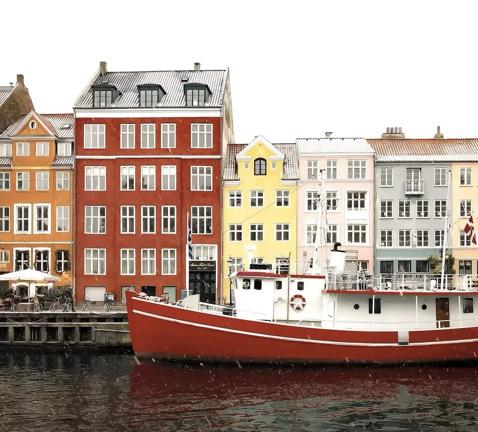 Farverige huse langs en kanal med en sejlbåd forankret i vandet.
