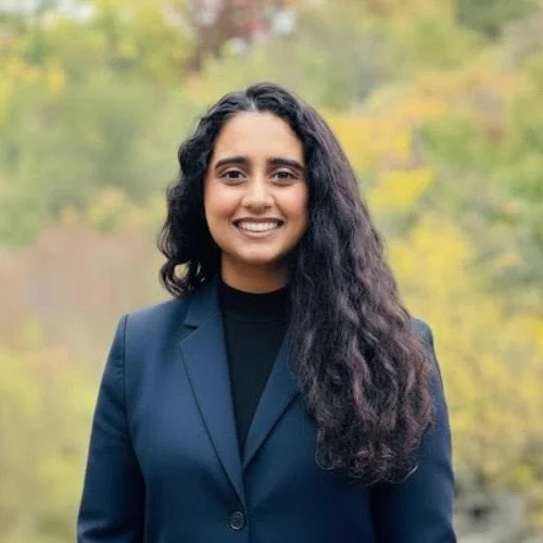 Young woman smiling outdoors with trees in the background.