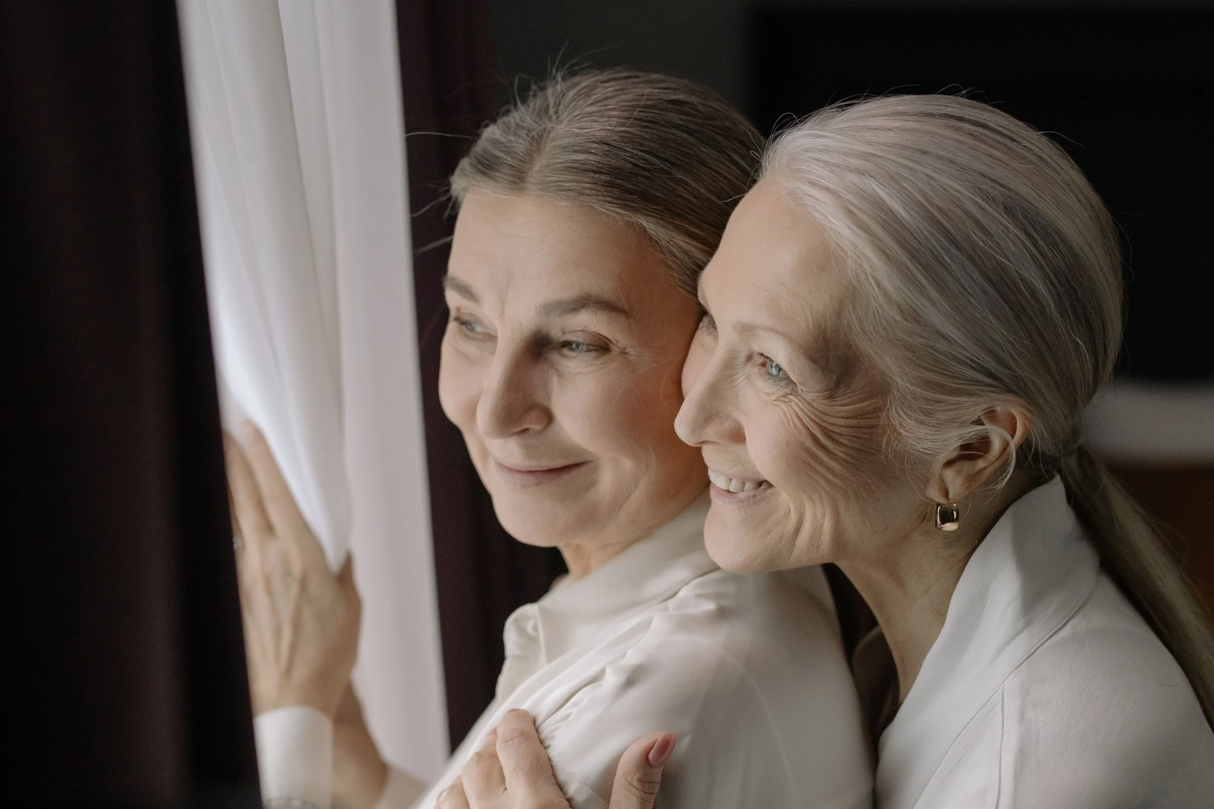 elderly lgbtq women couple smiling and embracing while looking out a window, showcasing love and happiness..jpg