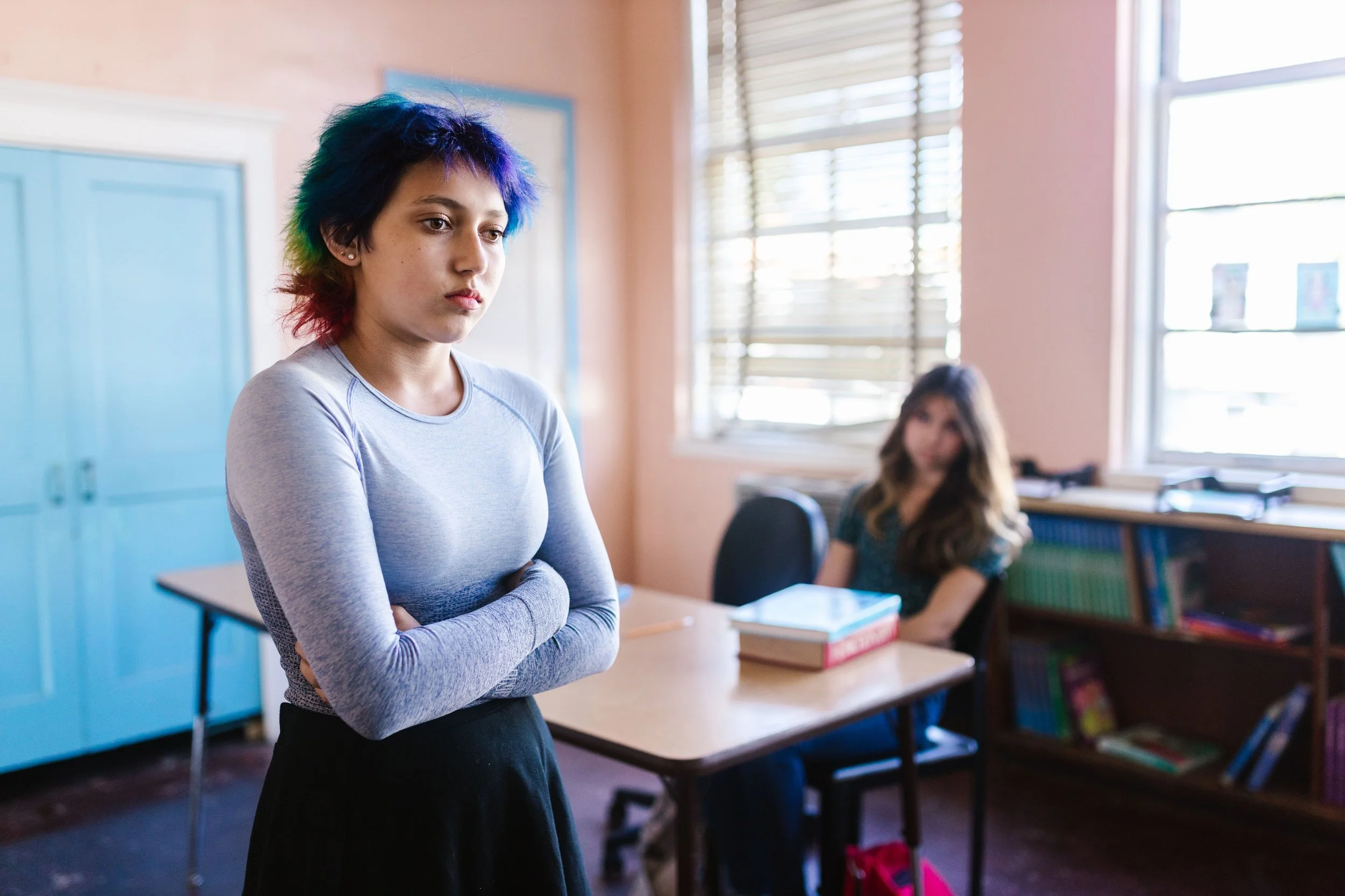 Student with vibrant hair crosses arms in school classroom
