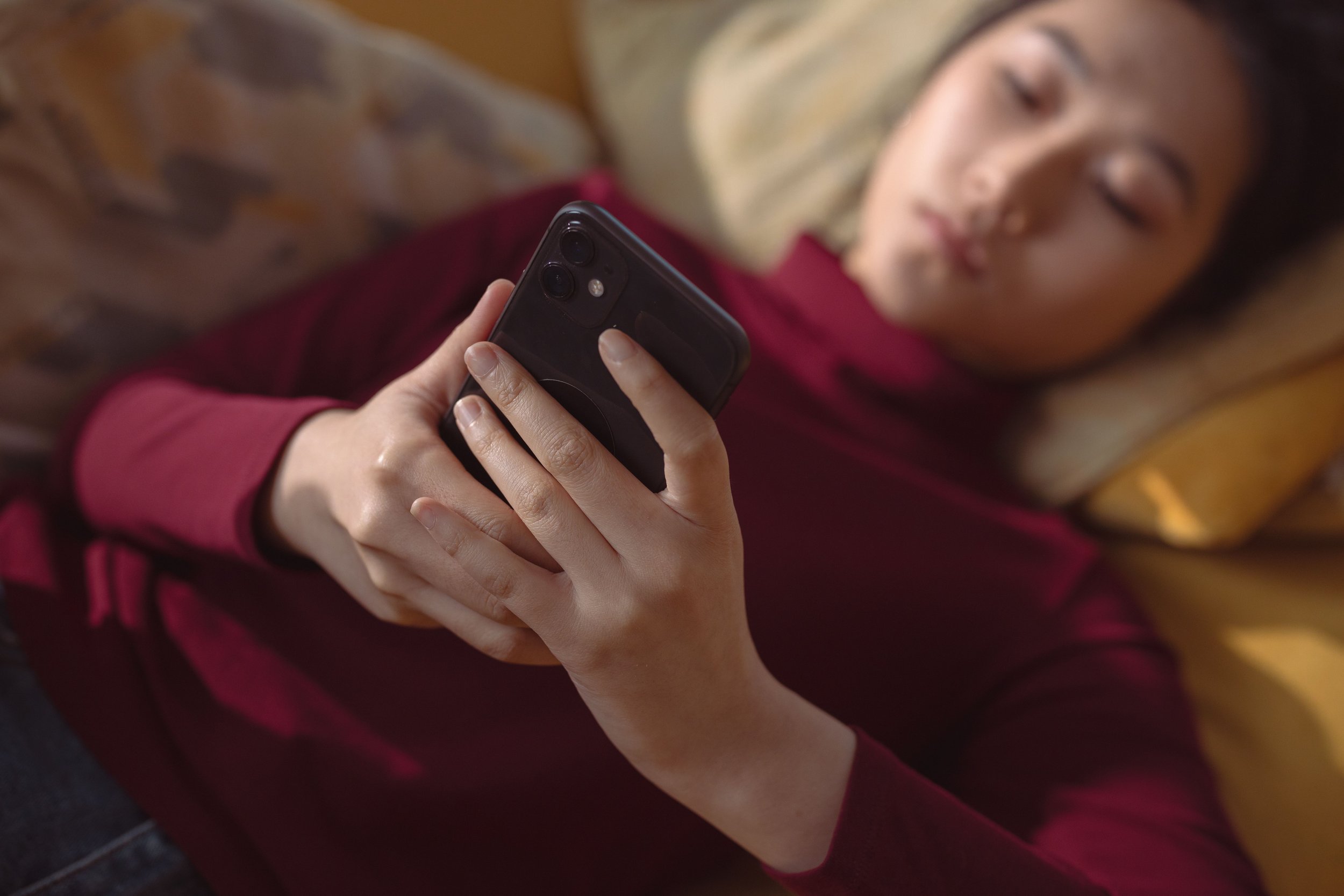 A young woman lying down, holding and using a smartphone for indoors