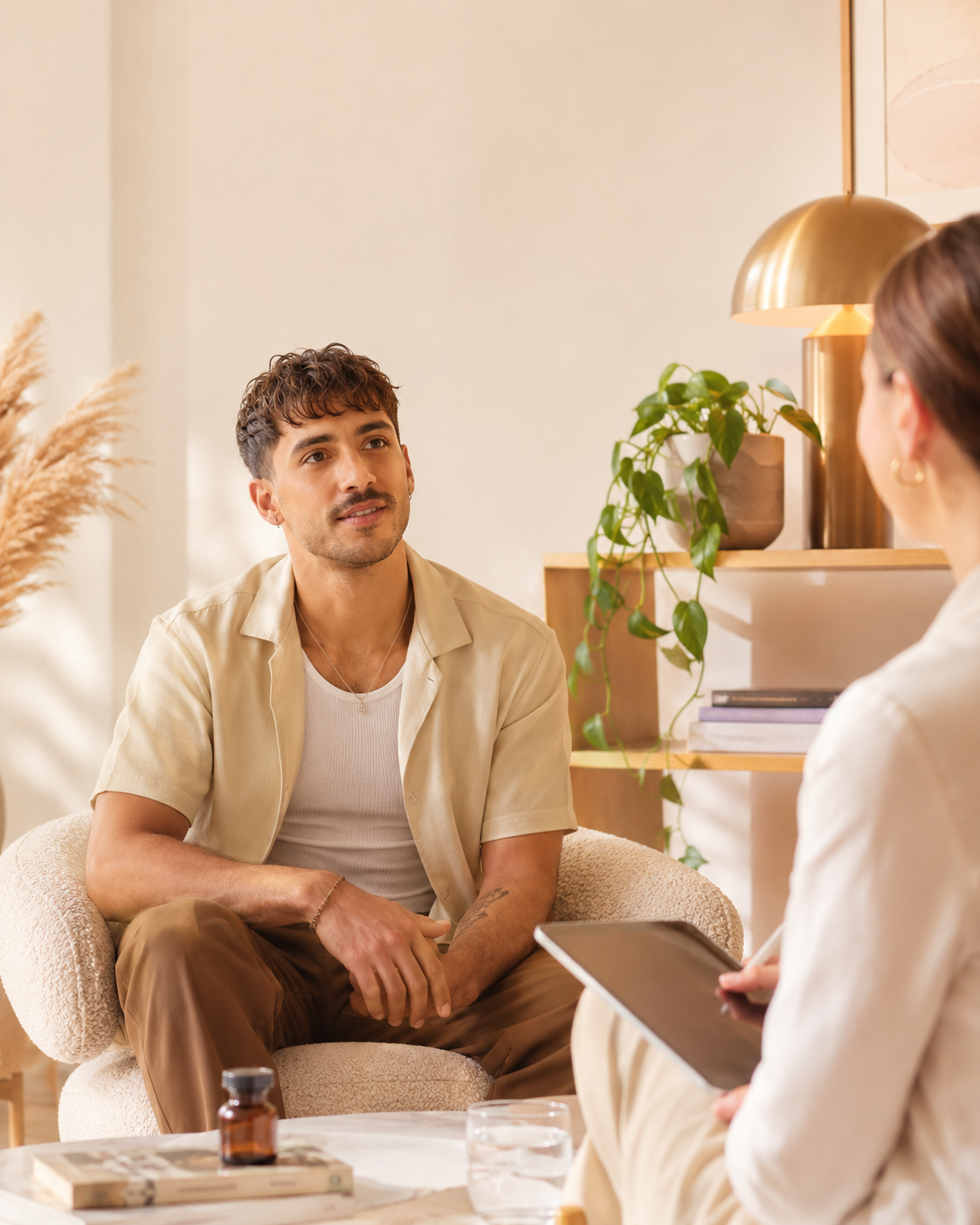 A man and a woman having a conversation in a cozy, well-decorated room with plants and a bookshelf.