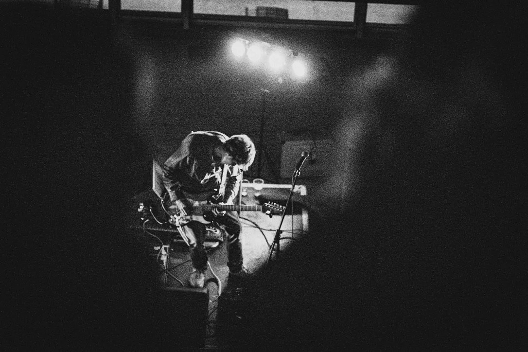 A musician playing an electric guitar on stage with bright lights overhead. 