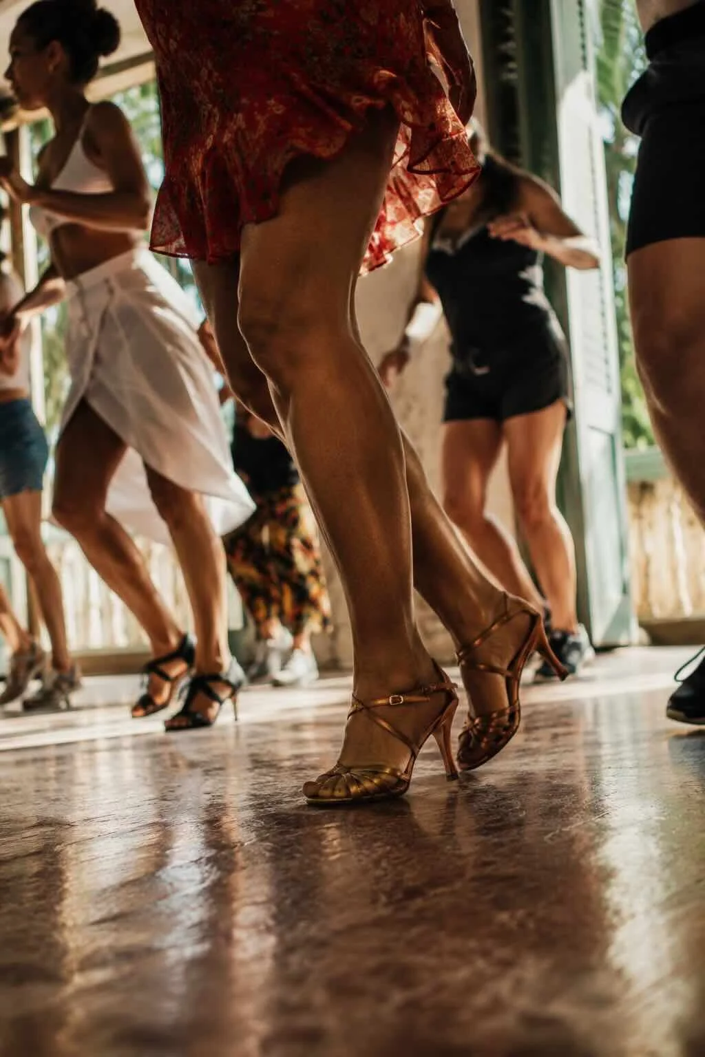 People dancing indoors, focus on a woman's legs in heels, with others visible in the background.