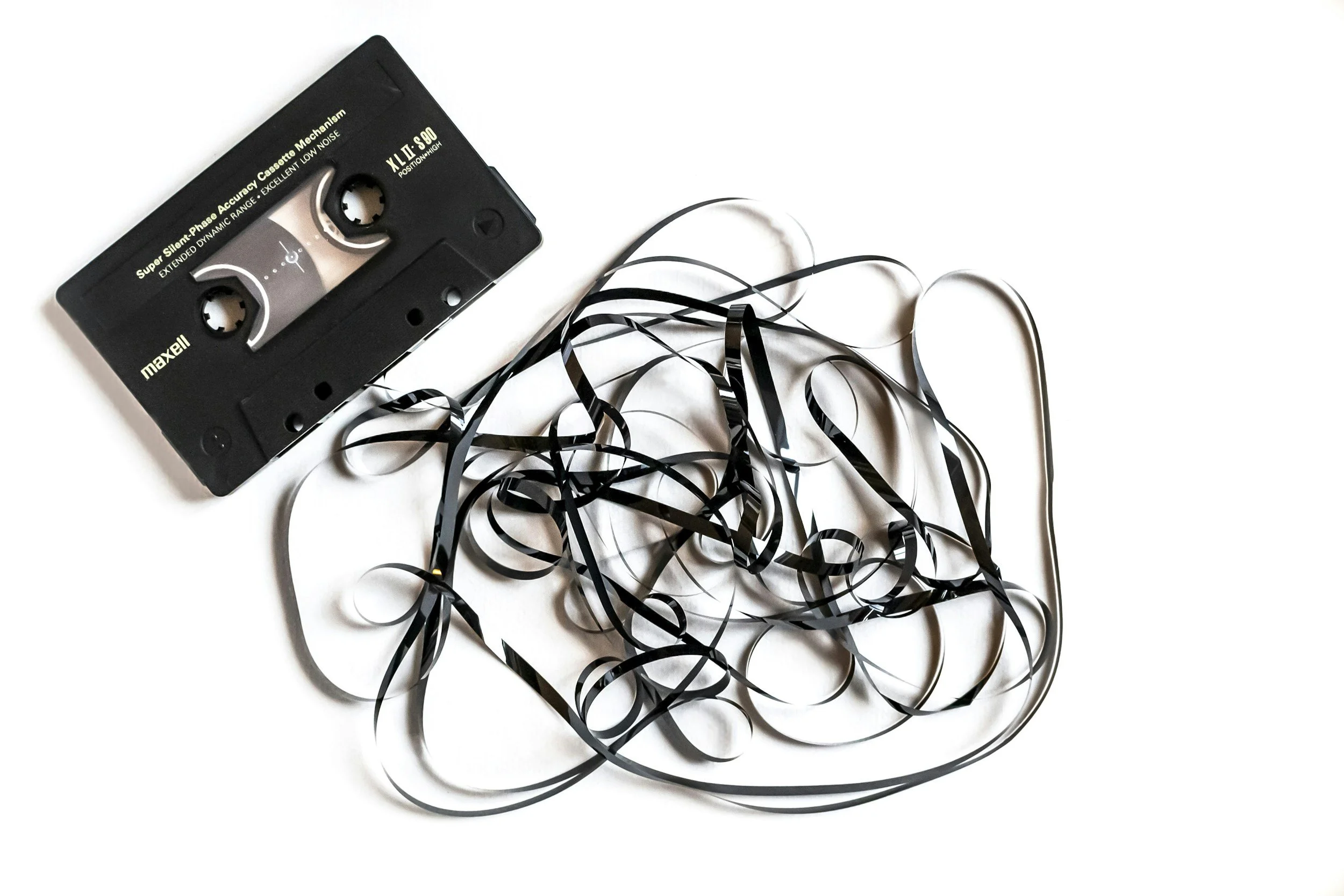 A black cassette tape with tangled black and silver ribbons scattered around it on a white background.