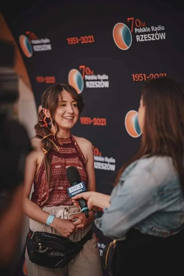 Young woman smiling during an interview at a Polish Radio event, with a microphone held up to her, standing in front of a backdrop celebrating 70 years of Polish Radio Rzeszów from 1951 to 2021.