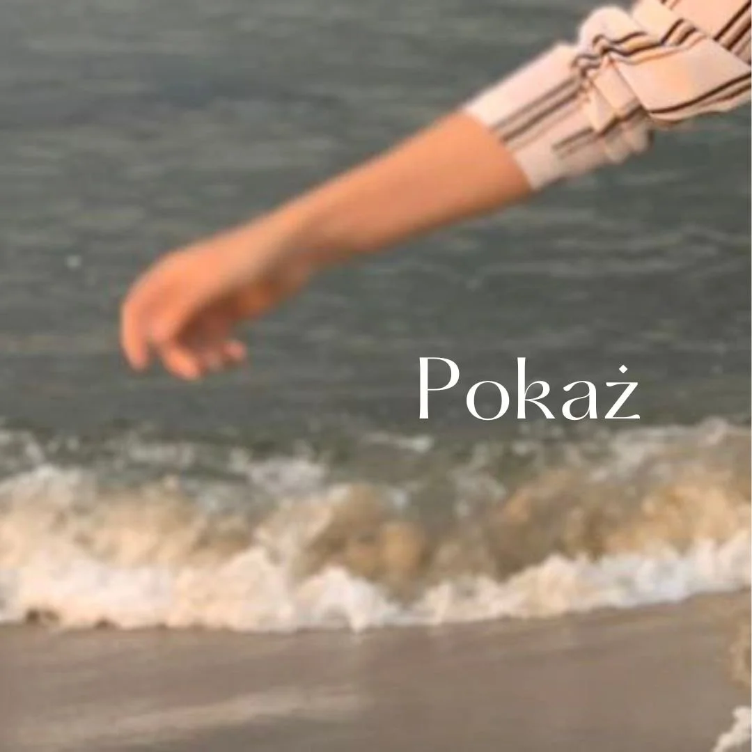 A person extending their arm and hand over the water at the beach, with waves in the background. The word 'Pokaż' is written across the image.