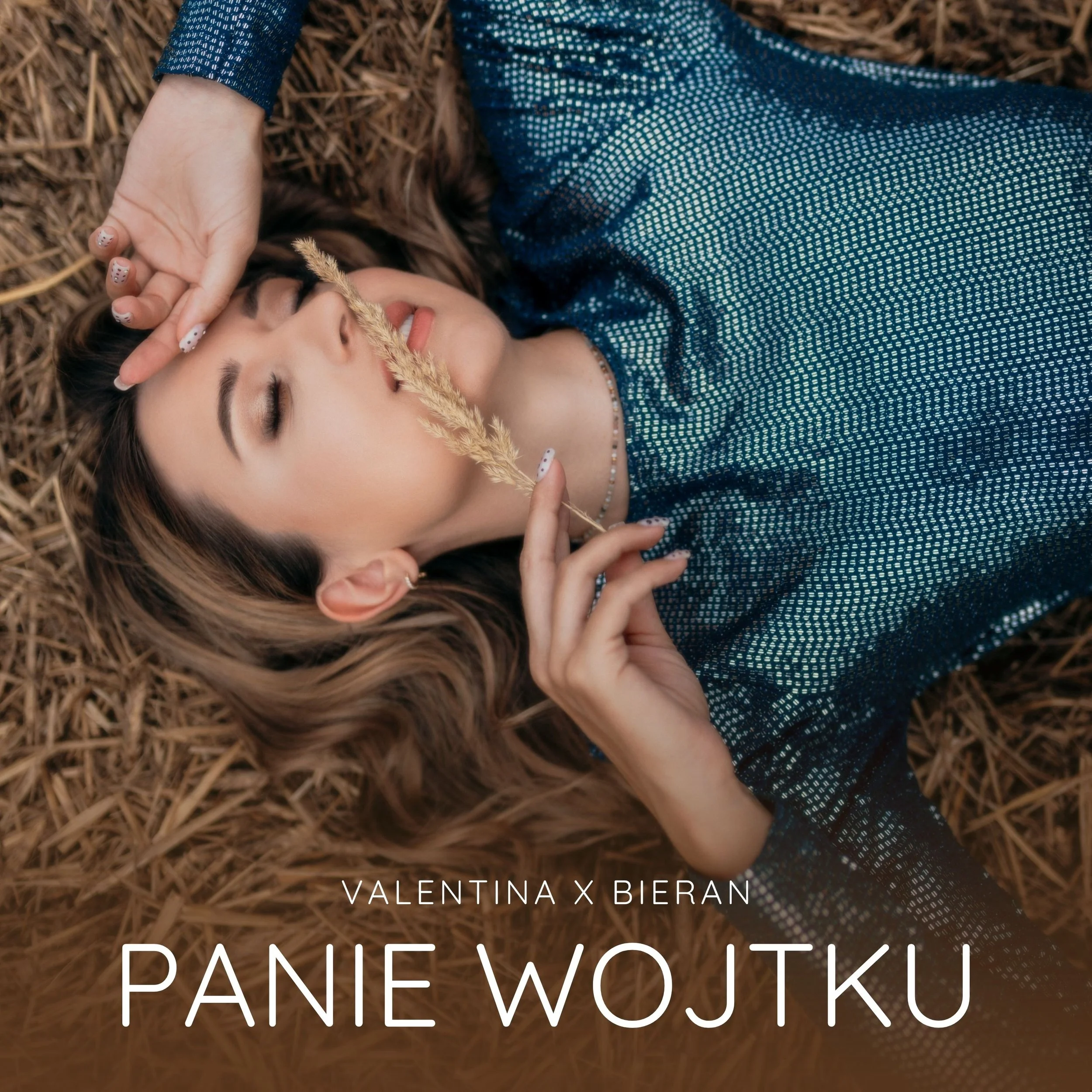 A woman laying on a bed of straw, holding a stalk of wheat near her face, with a relaxed expression, wearing a patterned blue dress, with text overlay including the names 'Valentina Pucin' and 'Danie Wojku'.
