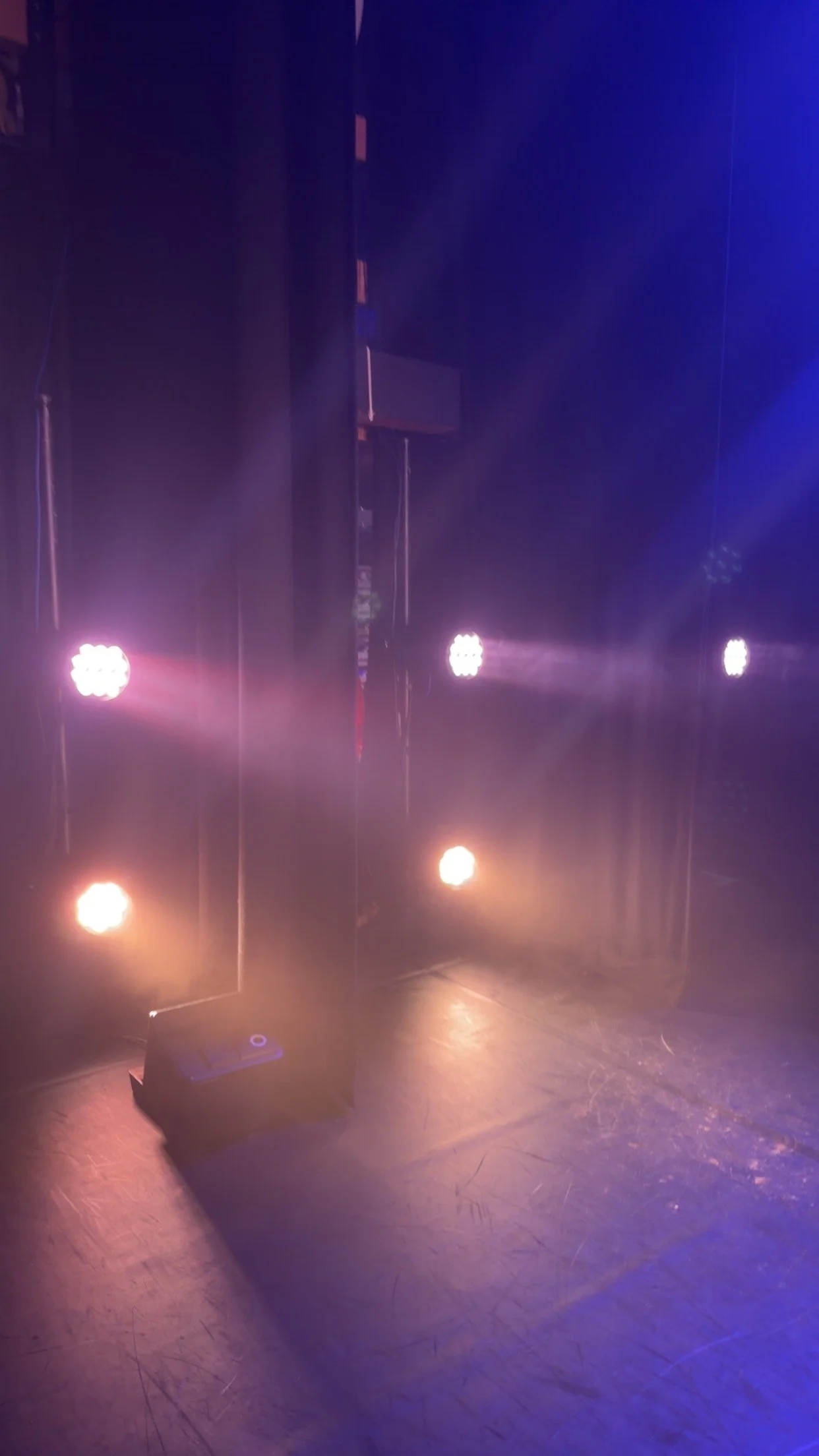 Stage with multiple bright colored lights shining on the floor and dark curtains in the background.