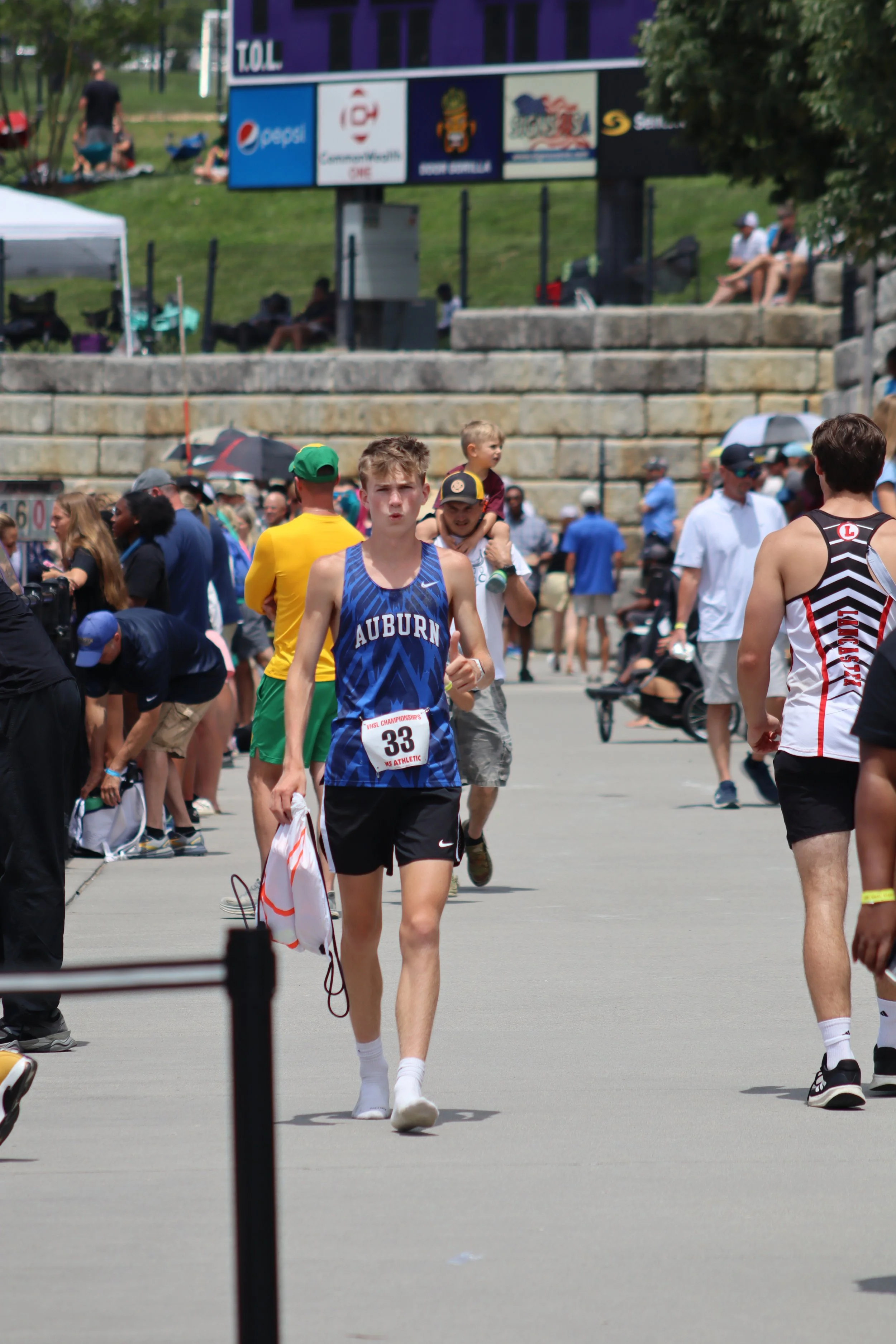 A runner with bib number 33 from Auburn University participating in a race, surrounded by other runners and spectators at an outdoor event on a sunny day.