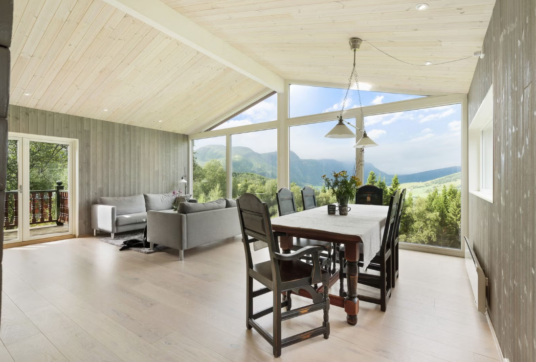 Bright living room with large windows showcasing a mountain view, featuring a dining table with chairs and a sofa.