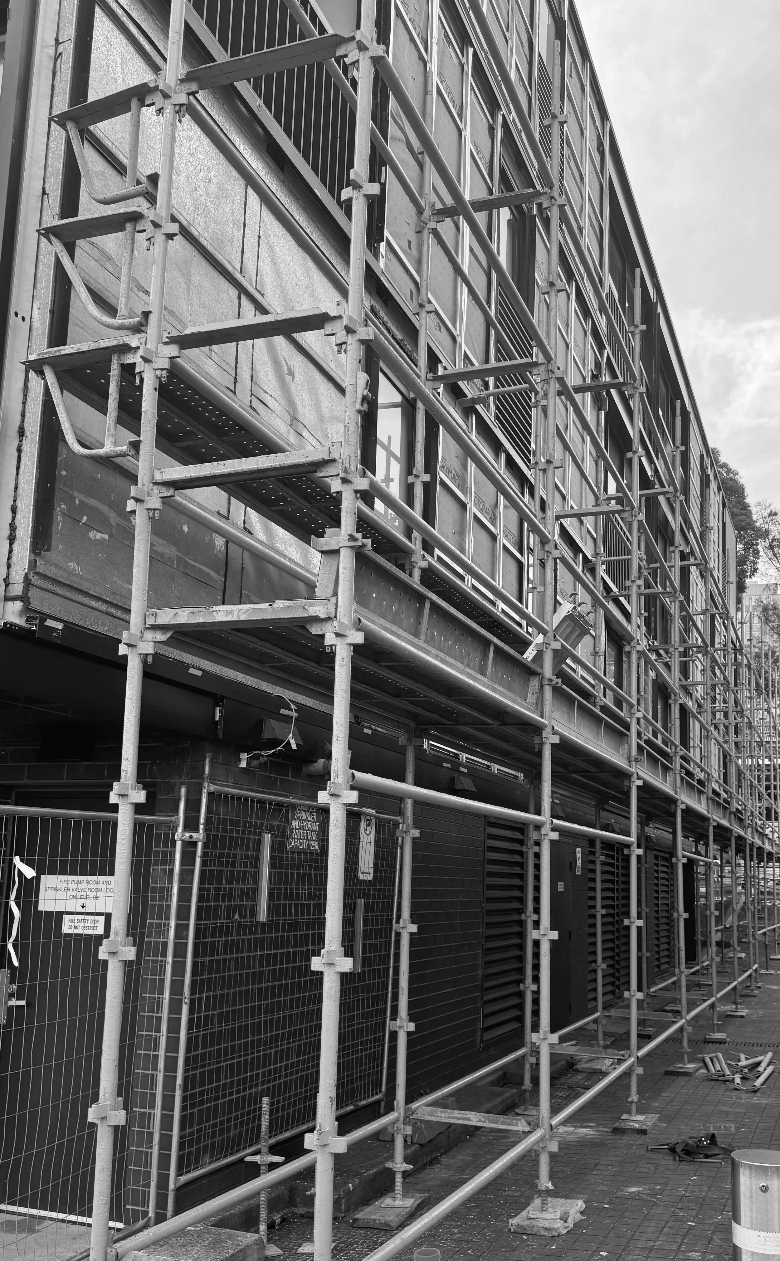 Construction site with scaffolding in front of a building under renovation, showing windows and some safety signs.