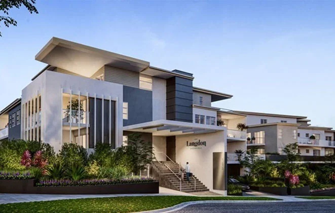 Modern multi-story apartment building with landscaped front yard and a person sitting on steps.