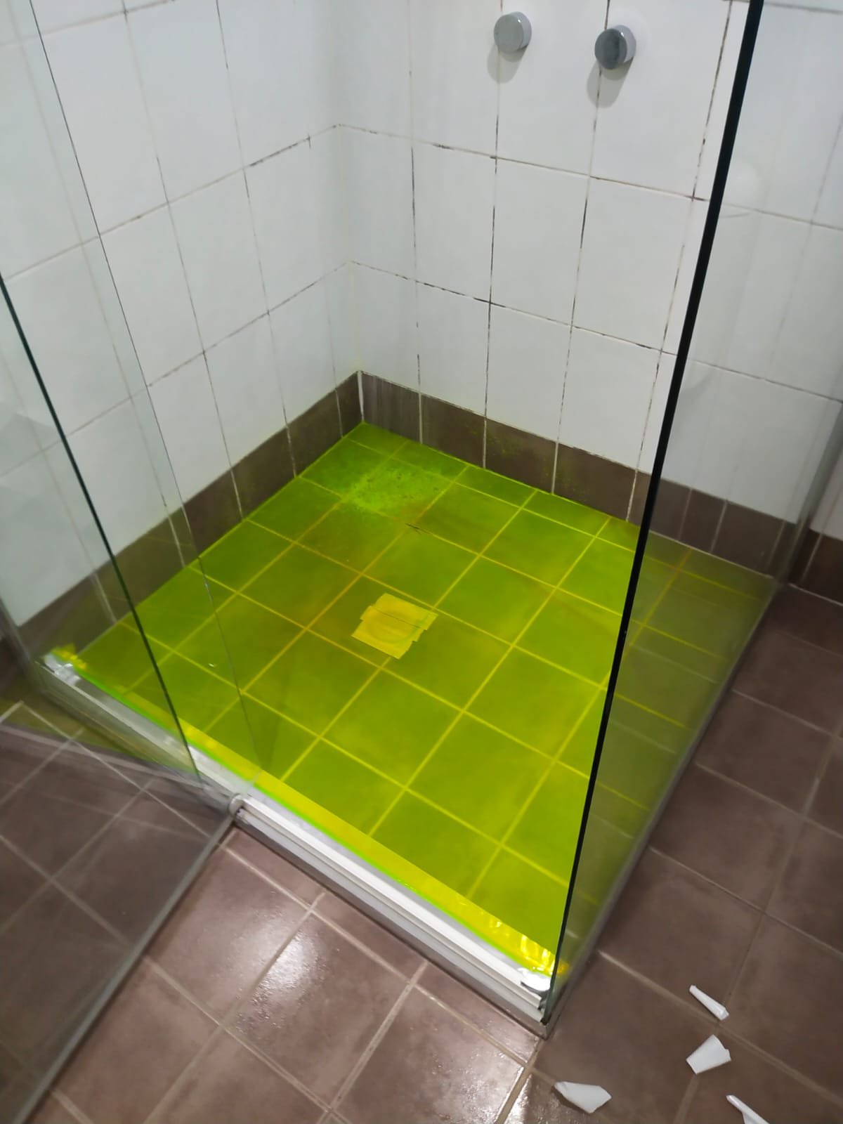 A shower stall with white tiled walls, a frosted glass door, and a yellow-green tiled floor with mold around the drain.