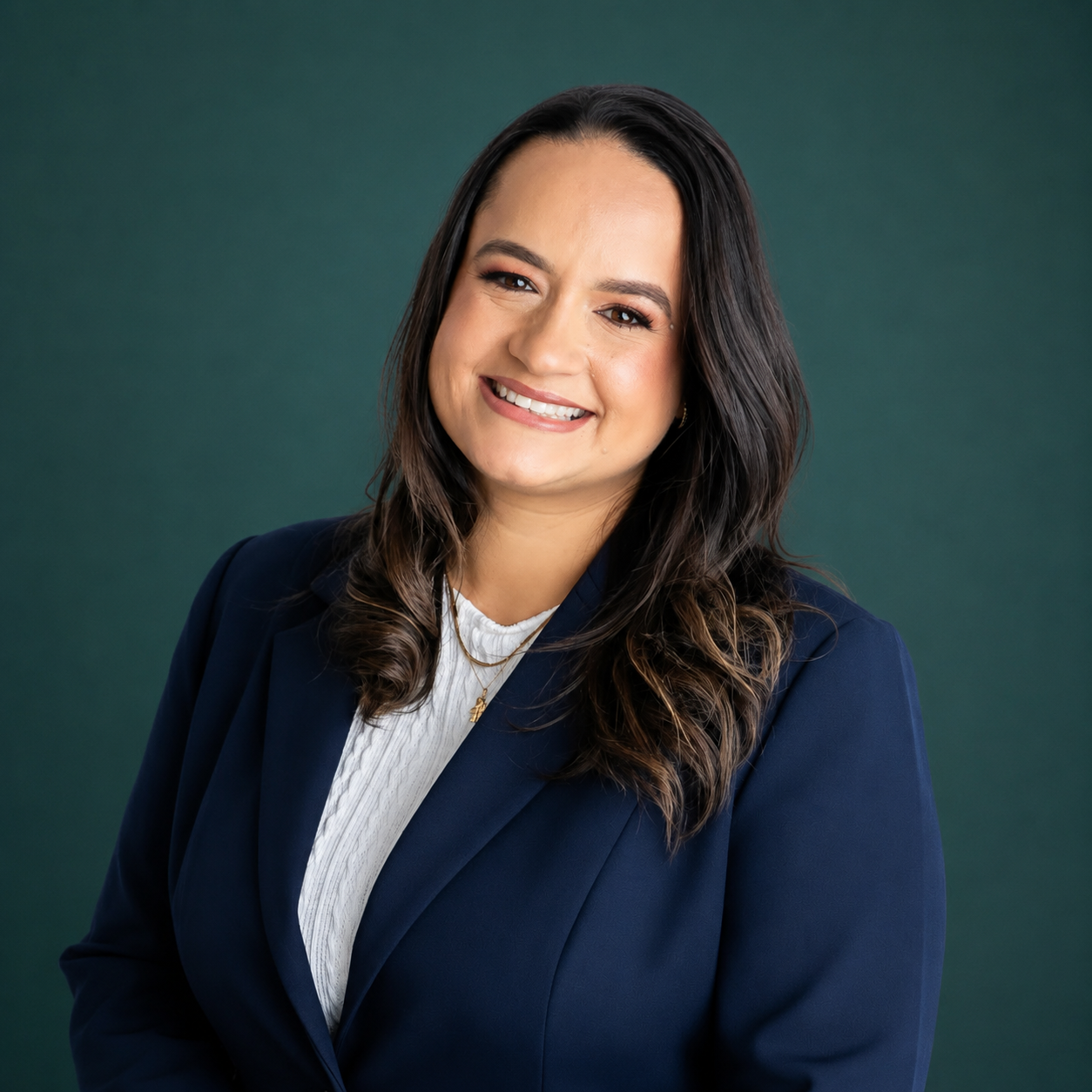 Mulher sorridente com cabelo castanho escuro, usando blazer azul e blusa branca, contra fundo verde
