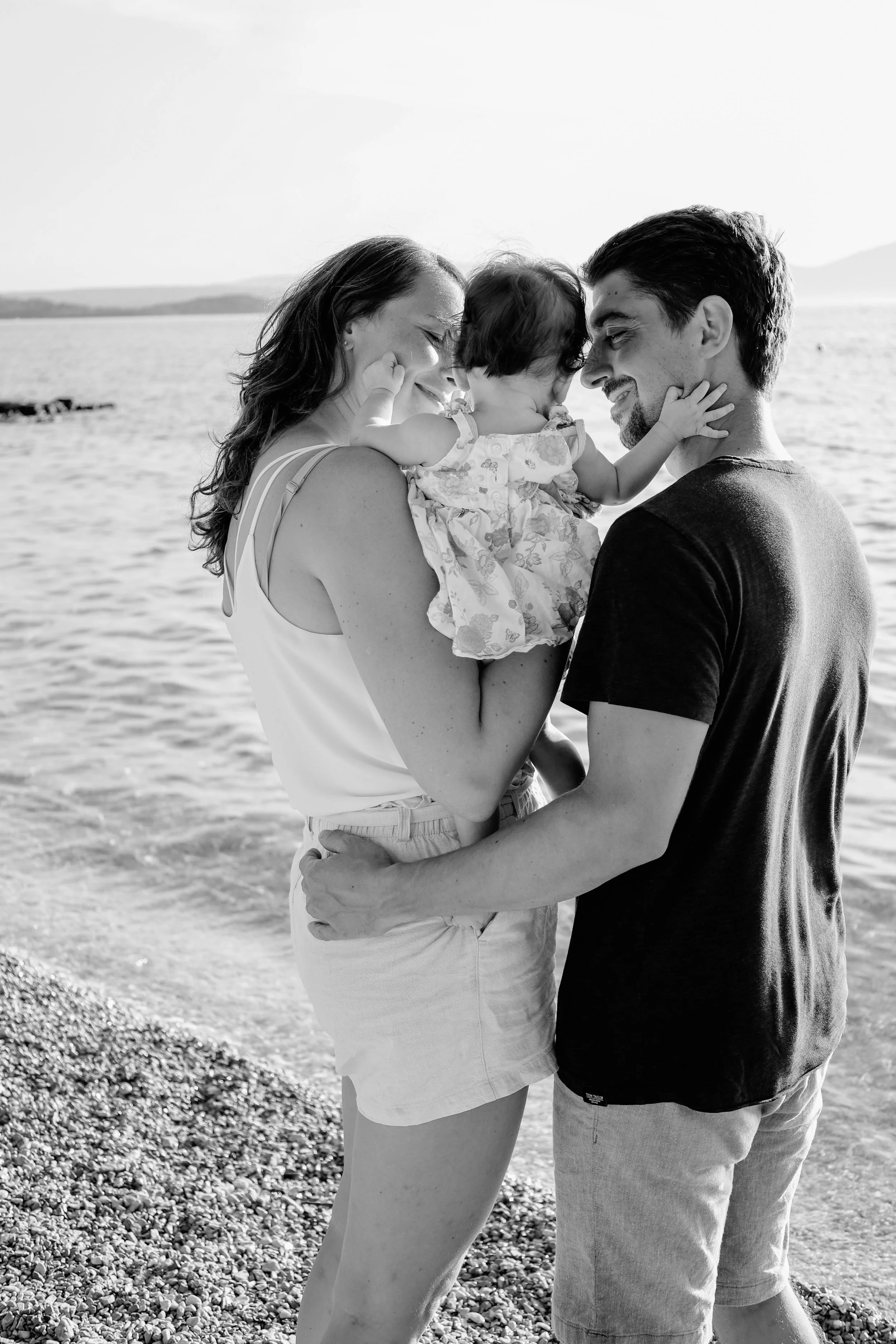 Ein glückliches Familienfoto von einer Mutter, einem Vater und einem Baby am Strand, alles in Schwarz-Weiß.