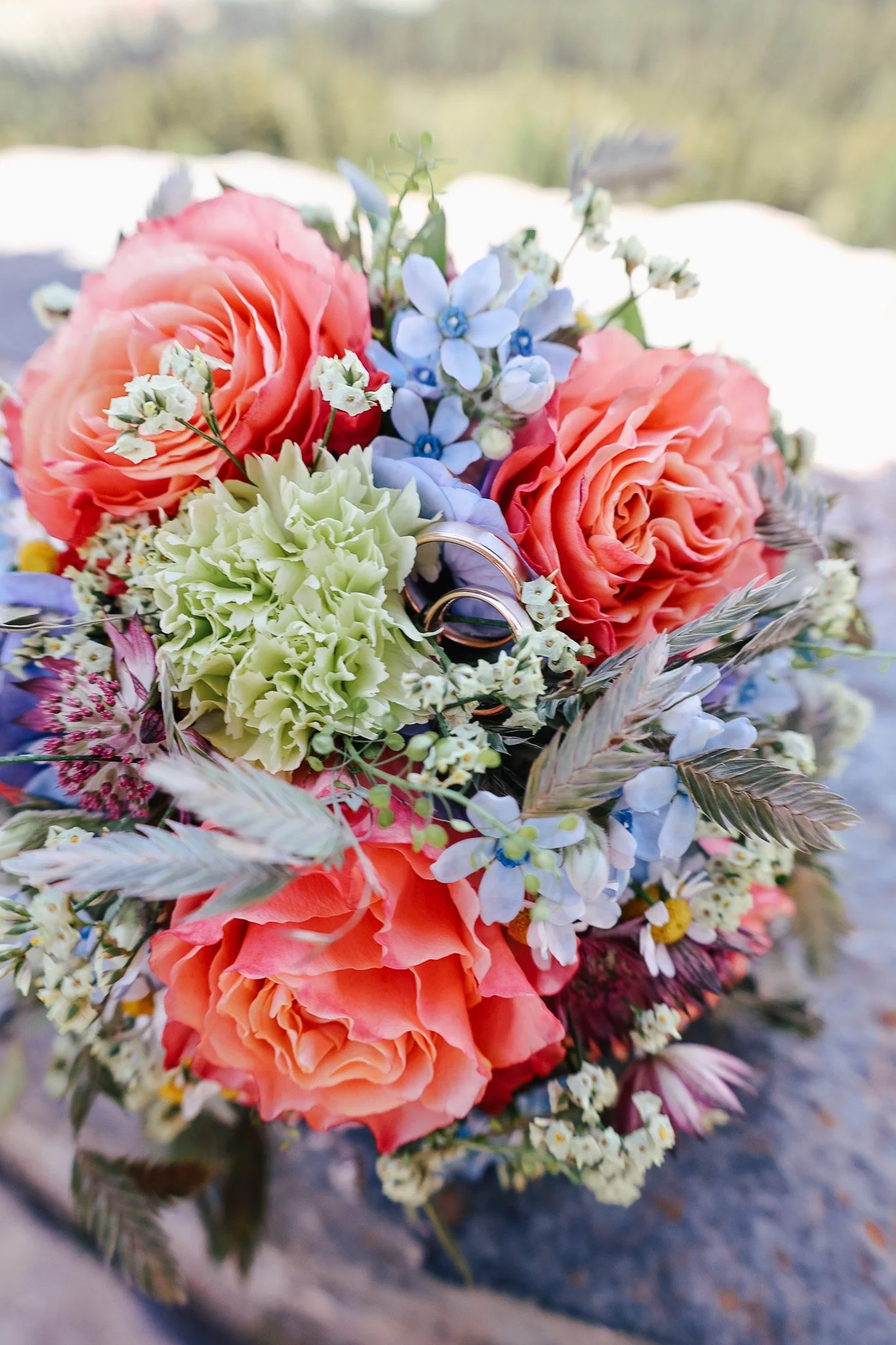 Ein Blumenstrauß mit rosanen Rosen, weißen Blümchen, grünen Hydrangea und anderen bunten Blumen auf einem Tisch.