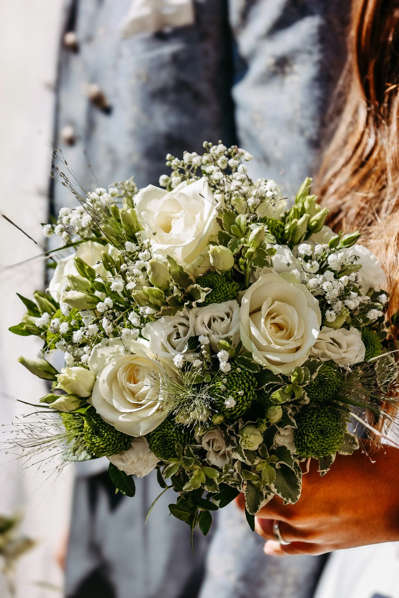 Person hält einen weißen Blumenstrauß mit Rosen, Schleierkraut und grünem Blumengrün in der Hand.