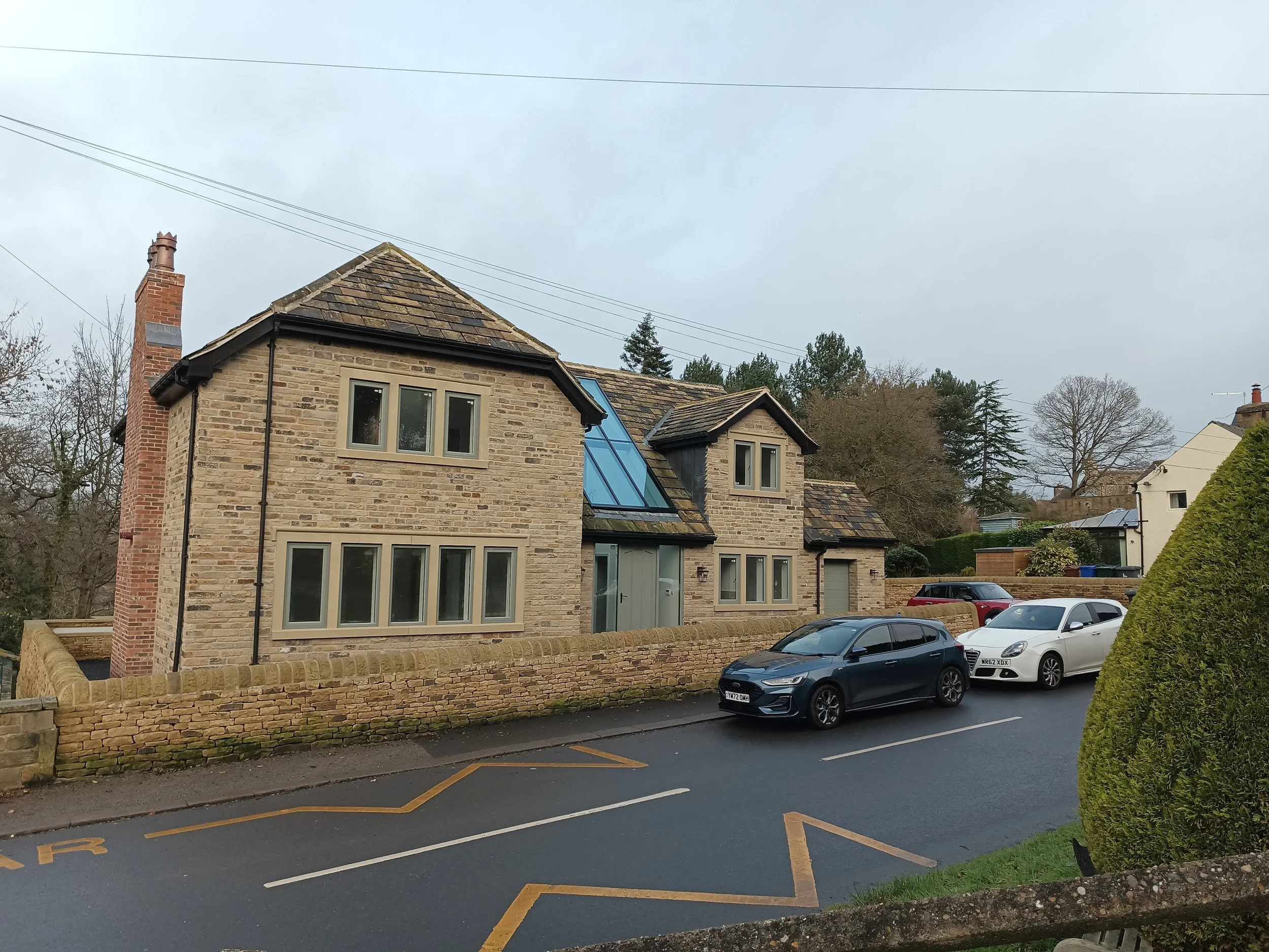 Street view of houses with brick and stone exteriors, parked cars, a brick wall, and overcast sky.