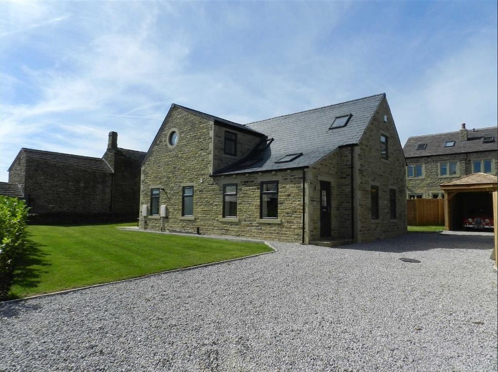 A modern stone house with a sloped roof, multiple windows, and a gravel driveway, located in a green yard under a clear, partly cloudy sky.
