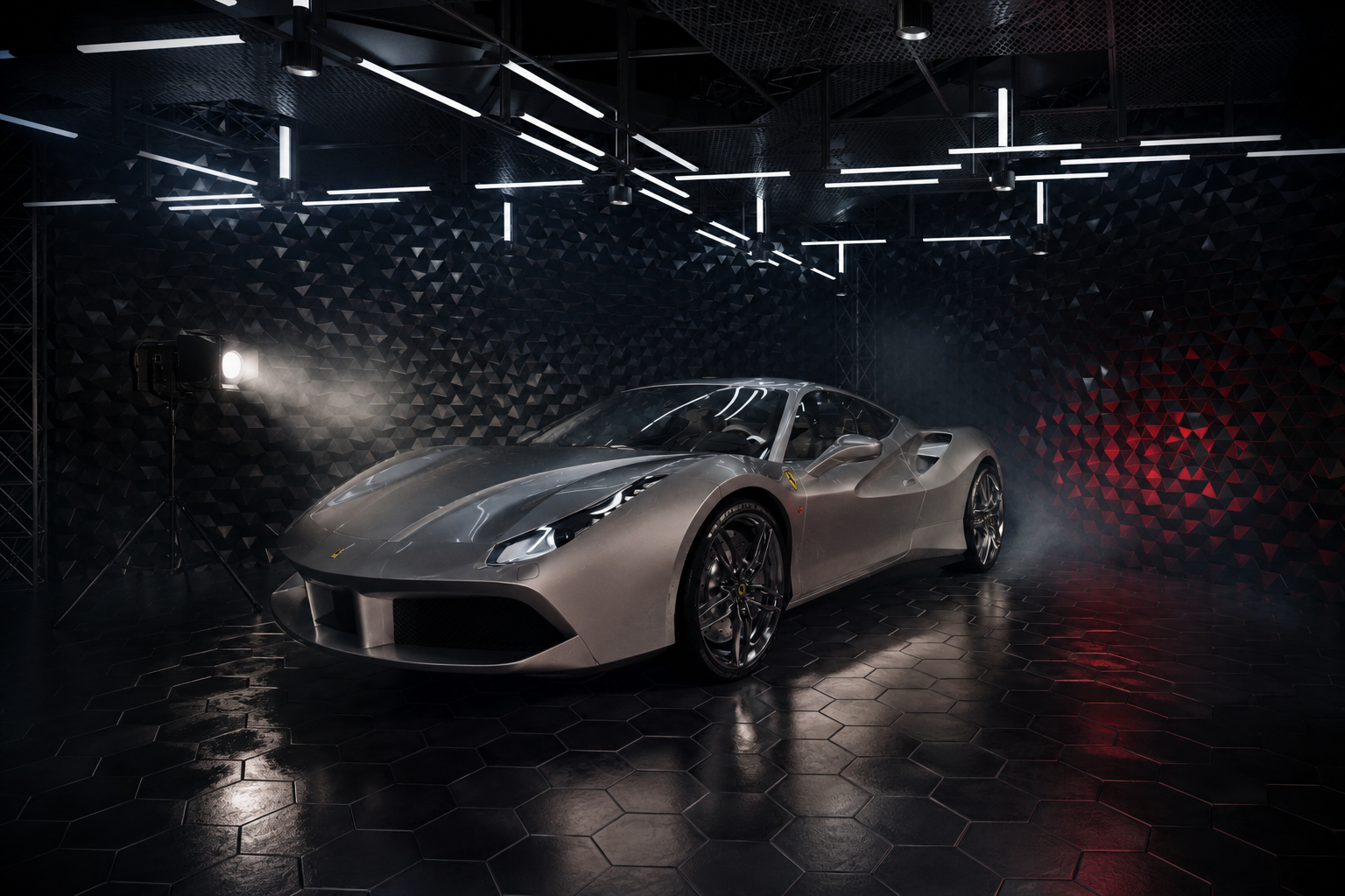 A sleek, silver sports car displayed in a dark, modern showroom with geometric black wall panels and hexagonal flooring, illuminated by overhead lighting.