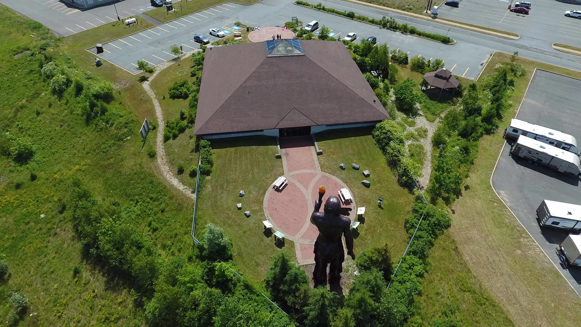 An aerial view of Millbrook Cultural and Heritage Centre, surrounded by trees and walkways, and adjacent parking lots with cars and recreational vehicles.