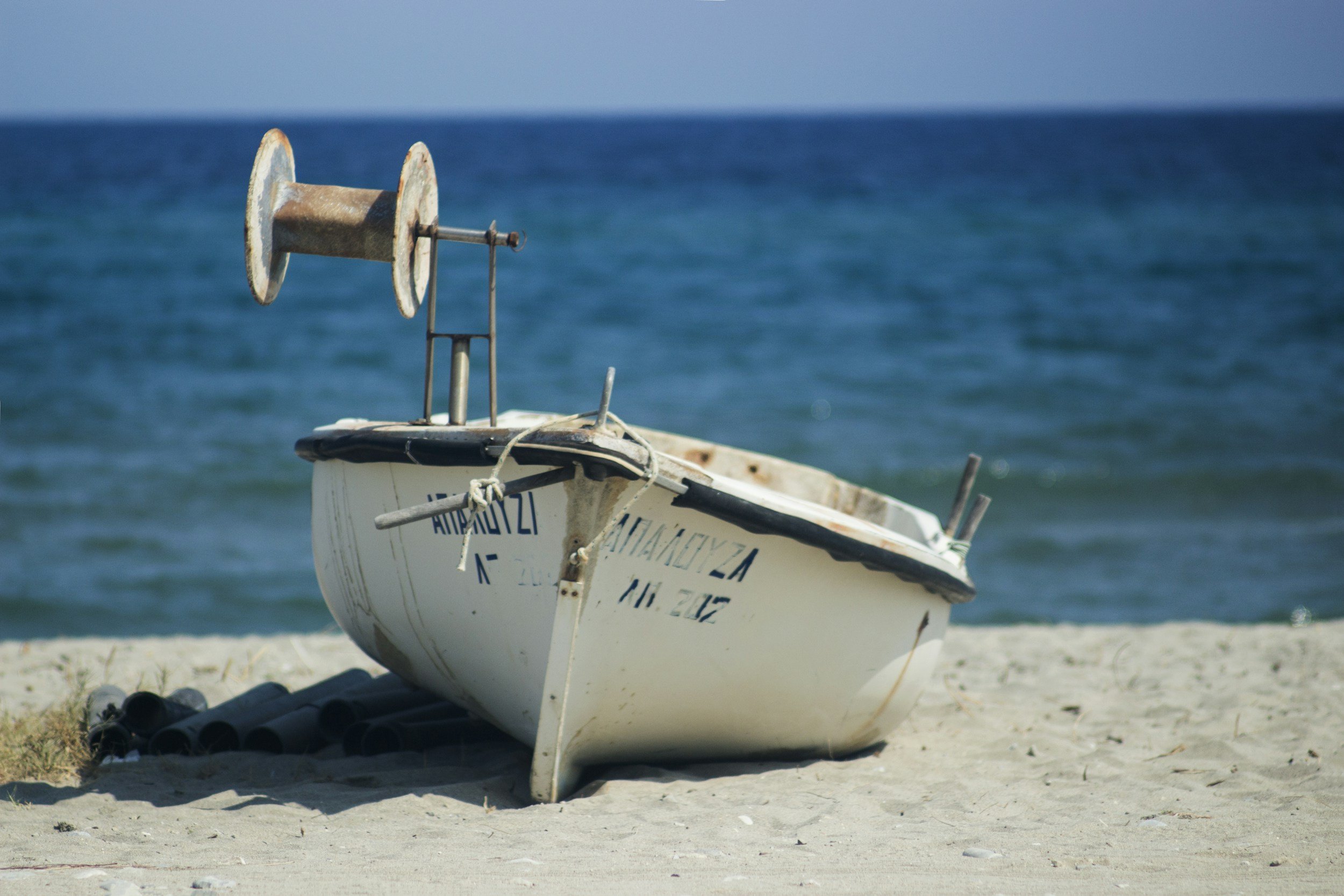 Rusty rowboat with equipment on a sandy beach, overlooking the ocean with a clear blue sky.