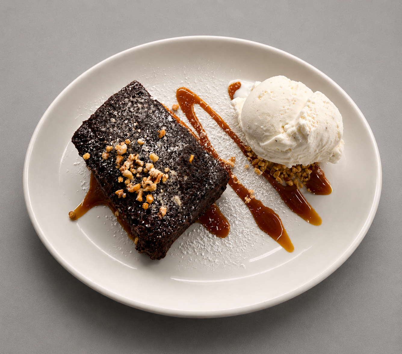 Postre de brownie de chocolate con nueces, helado de vainilla y caramelo en un plato ovalado blanco