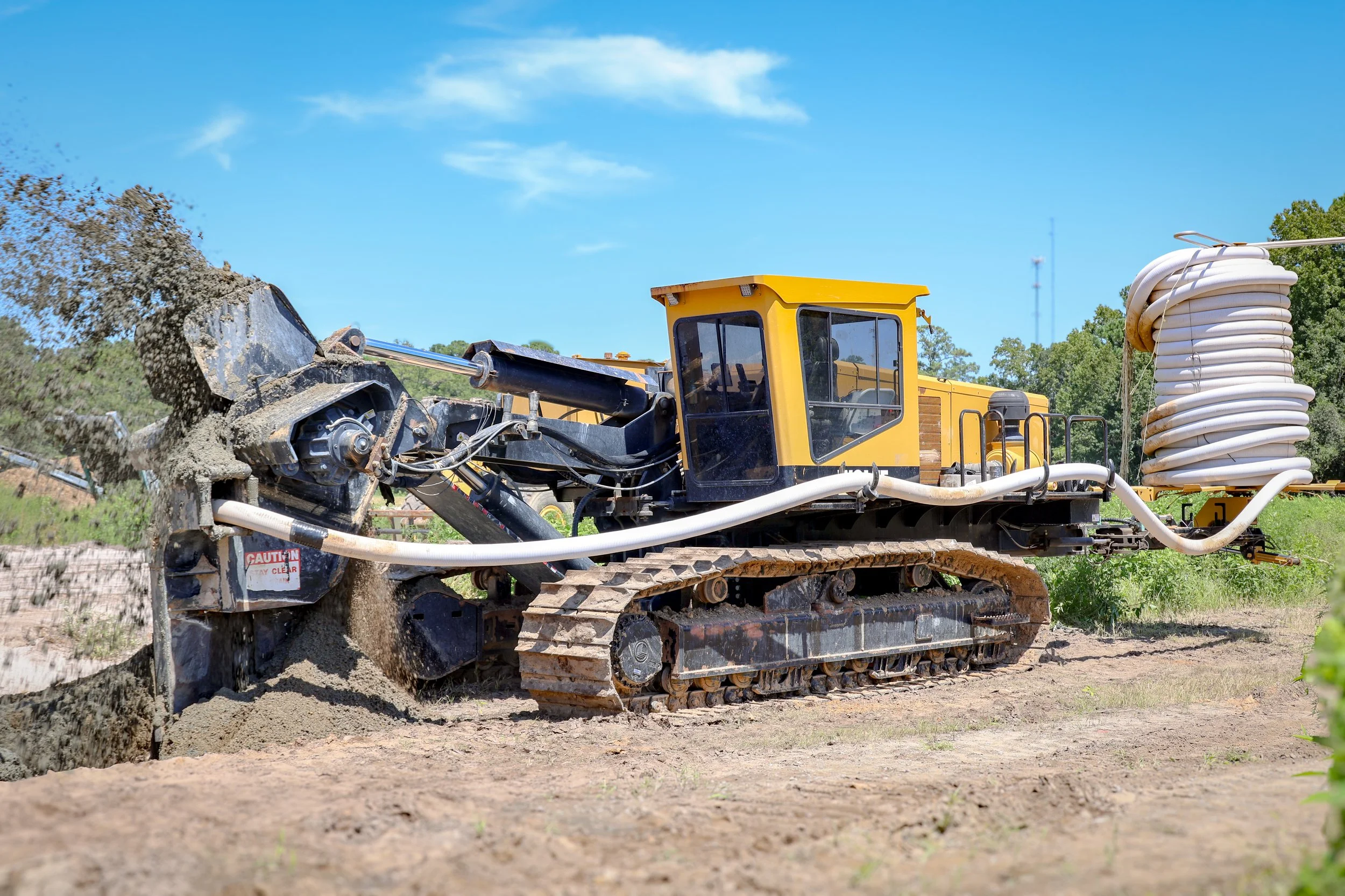 A yellow bulldozer moving dirt on a construction site with blue sky and green trees in the background. (JF Pedersen Co)