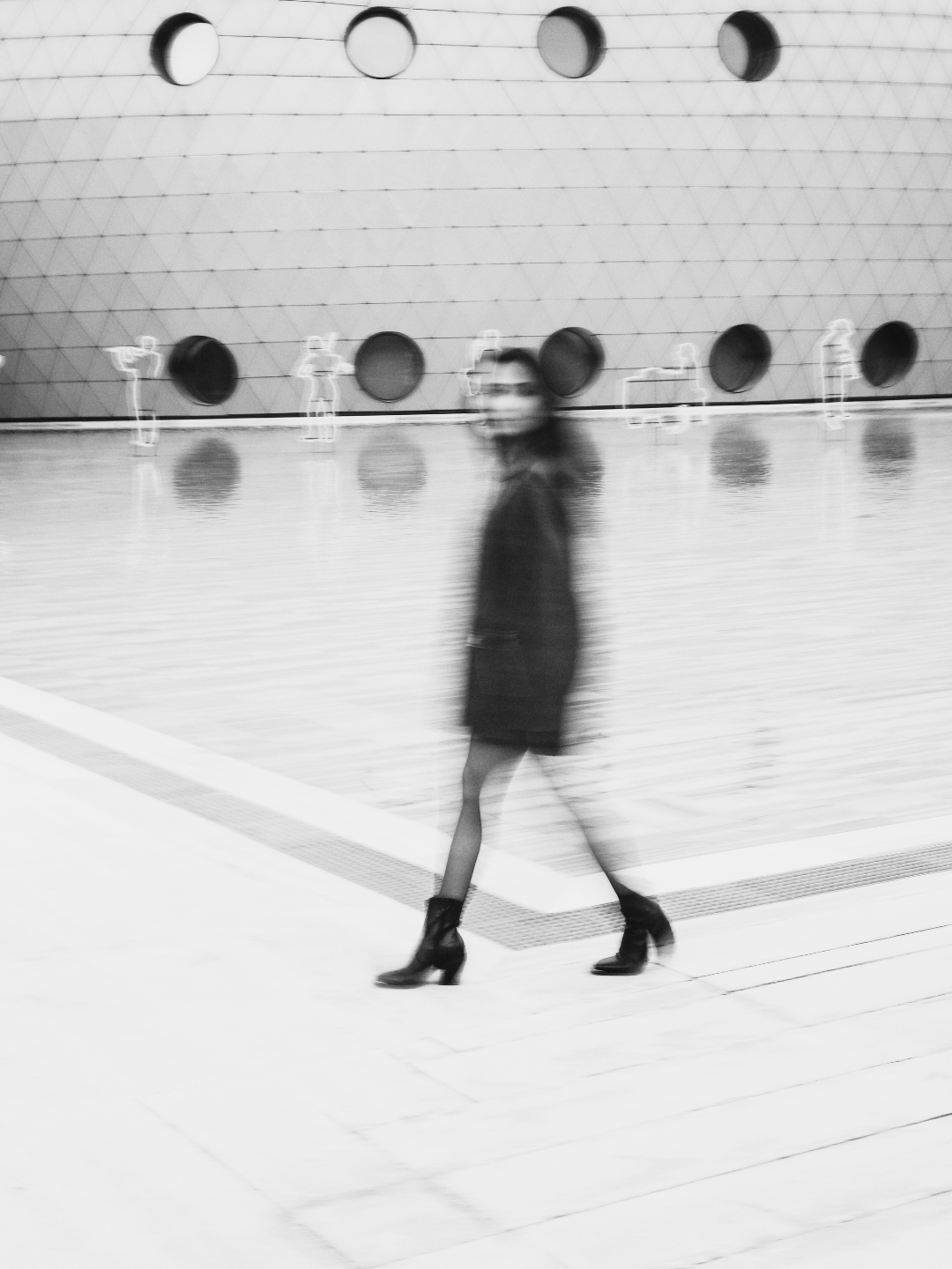 Blurred black and white image of a woman walking through a modern architectural space — evoking the invisible signals and buyer behavior patterns analyzed by Smith + Soma.