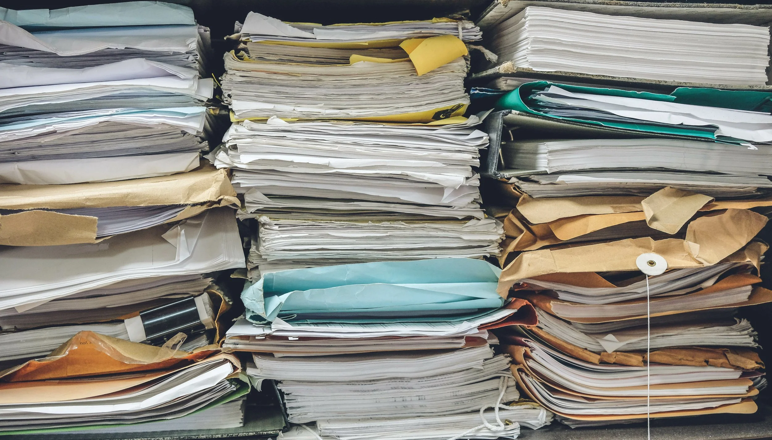 Stacks of crumpled and folded papers, some in envelopes, on shelves.