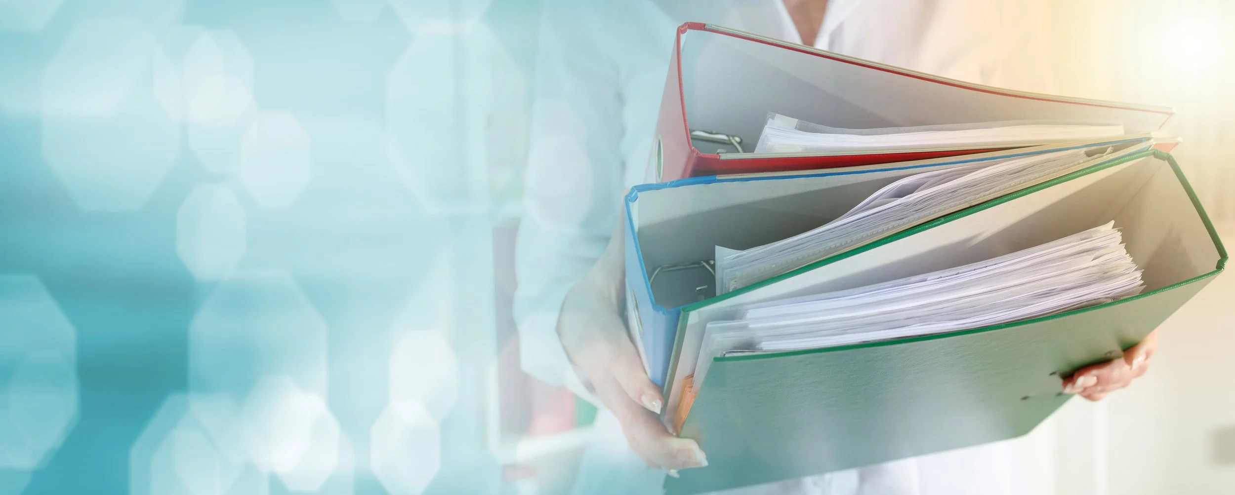 Person holding a stack of colorful binders and papers, with a blurred background of office environment and light effects.