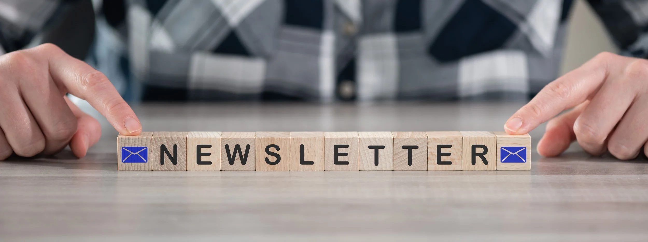Hands placing letter blocks spelling 'NEWSLETTER' on a table, with blue email icons on the outer blocks.