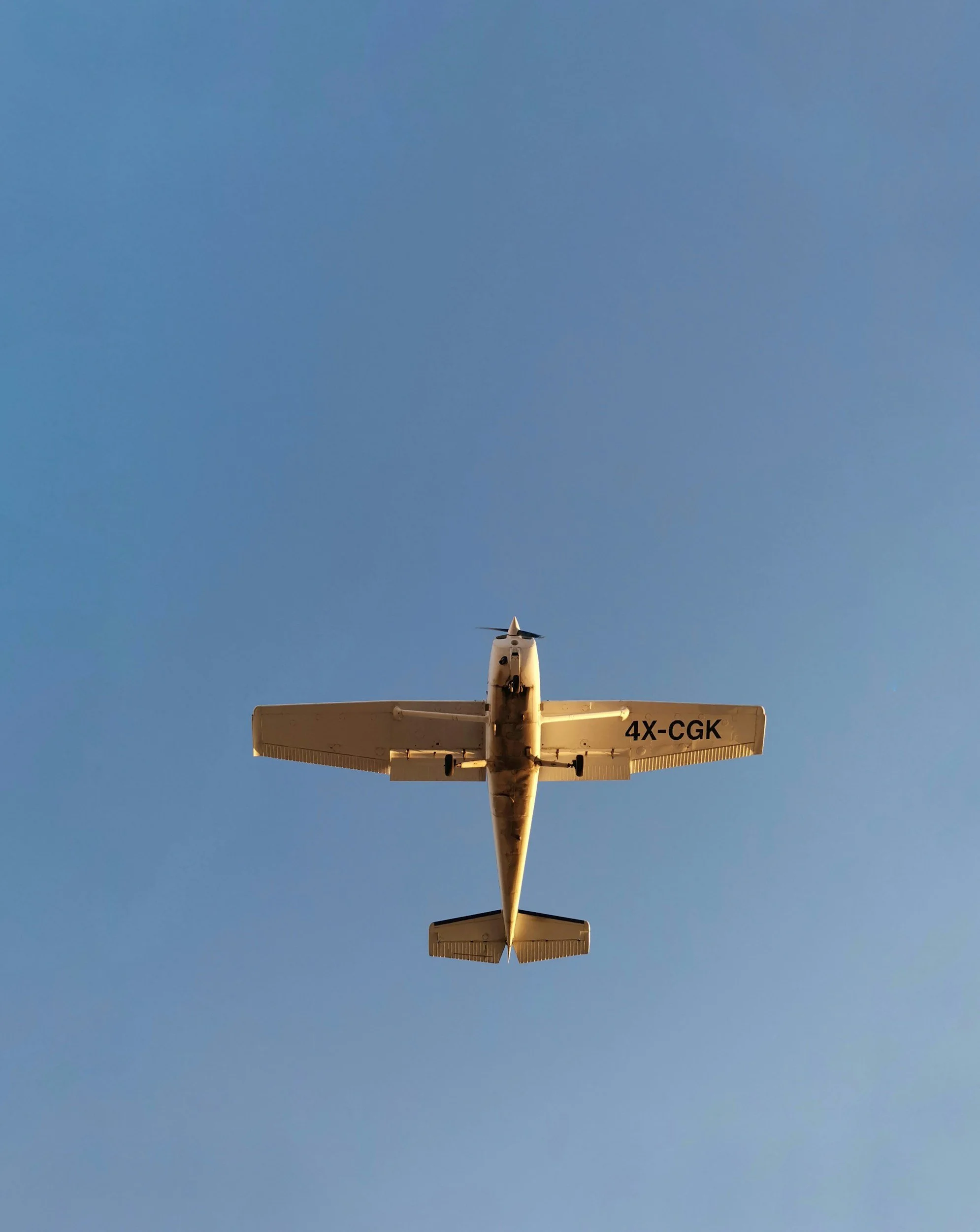 A small airplane flying in the clear blue sky, with the underside visible showing the registration number 4X-CGK.