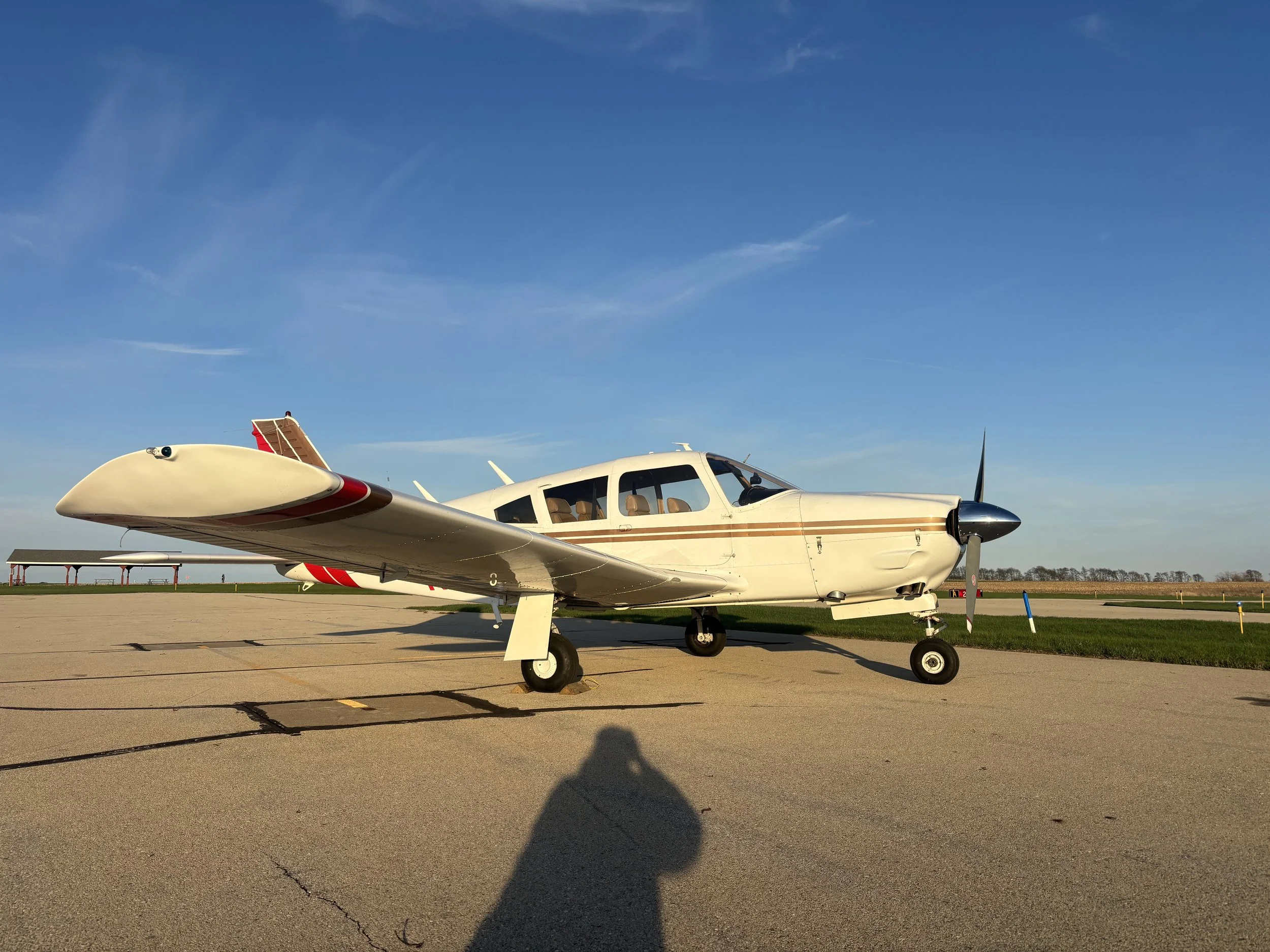 Small private airplane parked on an airport tarmac with a blue sky and some clouds overhead.
