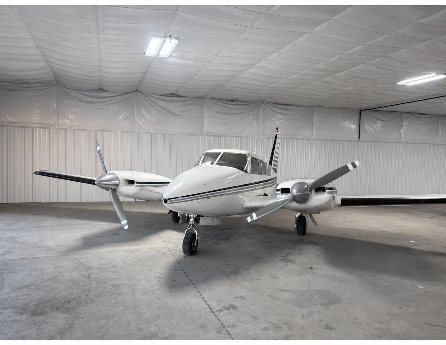 A white twin-engine propeller airplane inside a spacious hangar with white walls and ceiling.