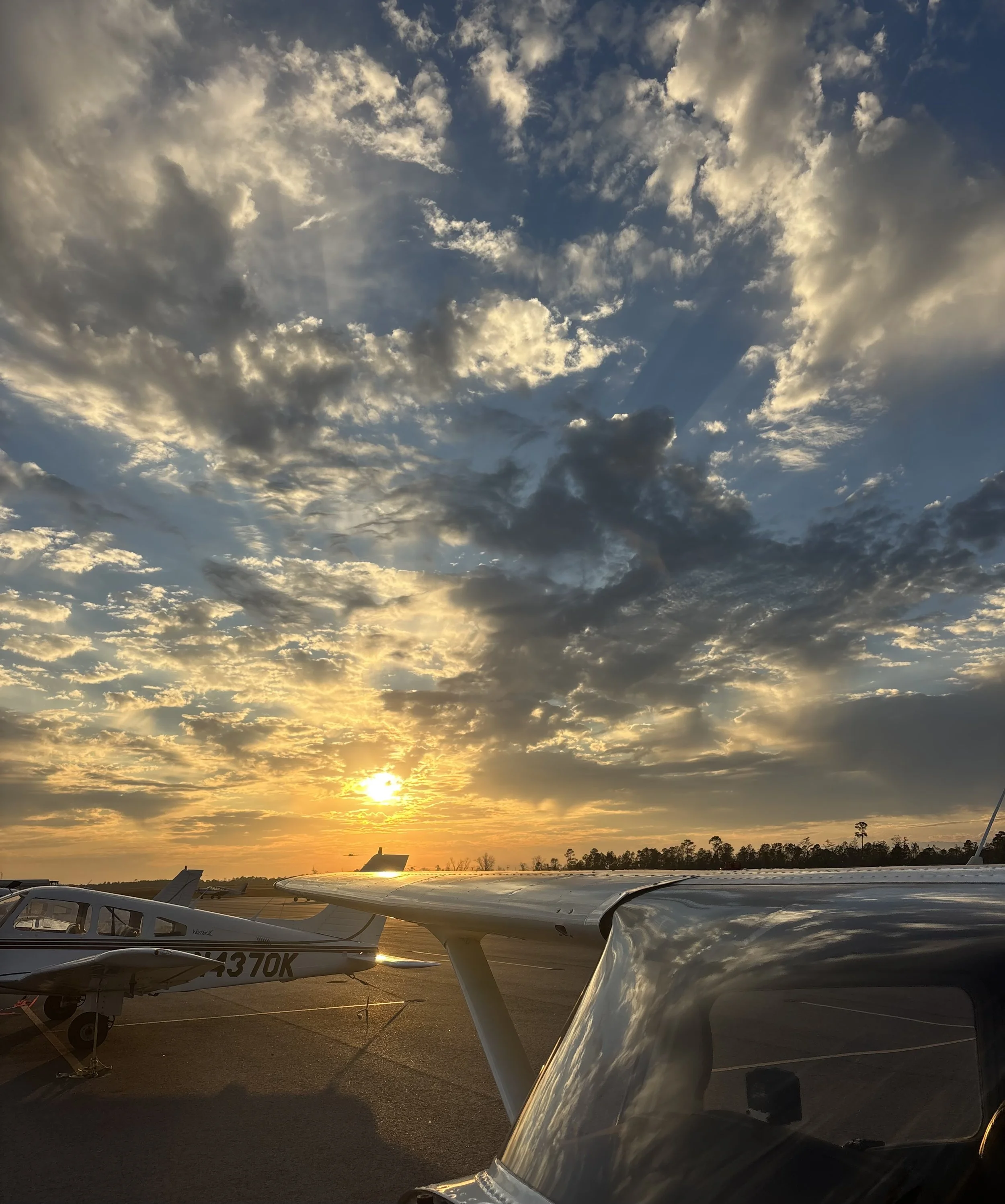 Small aircraft parked on tarmac at sunset with partly cloudy sky overhead.